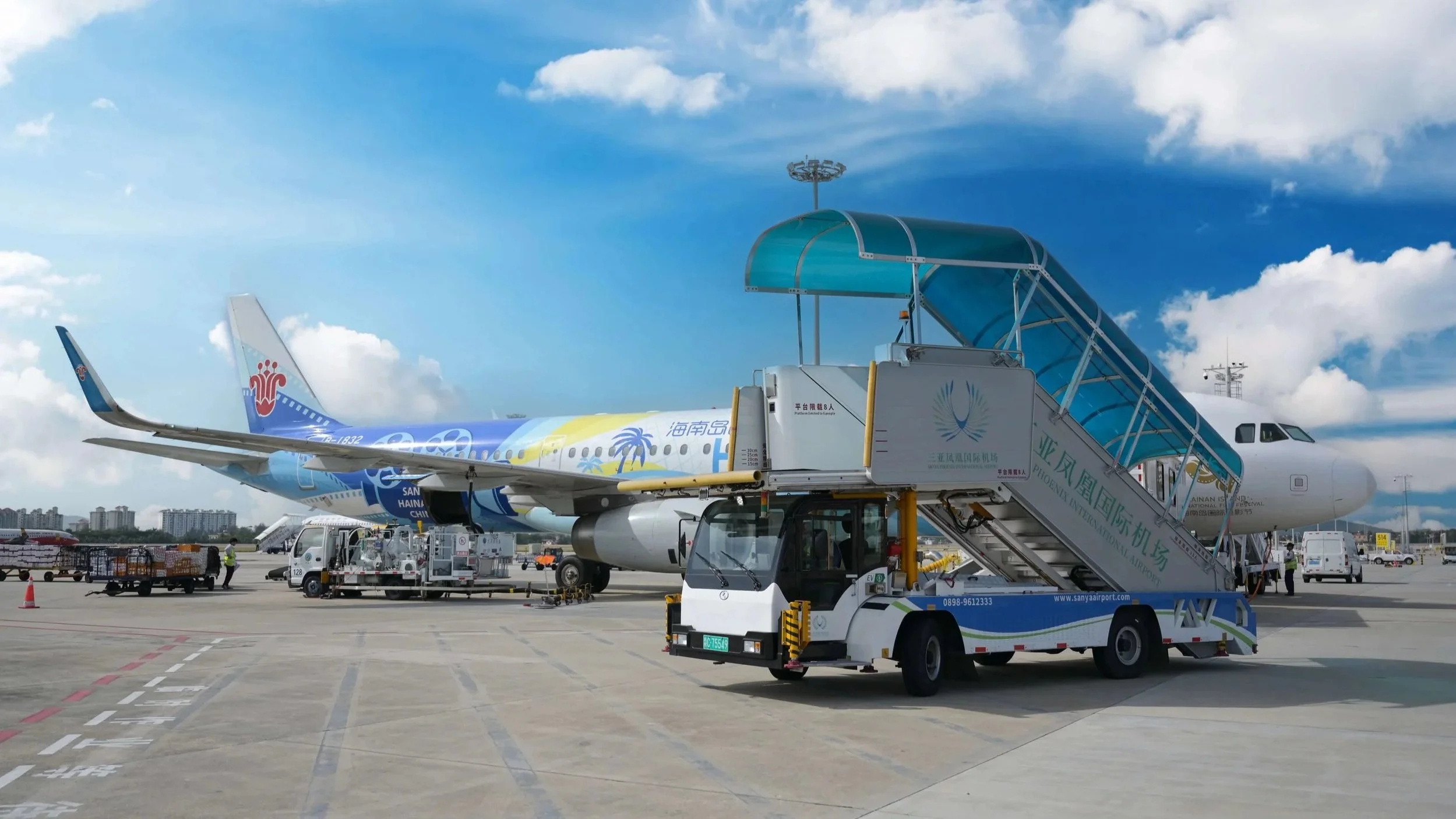 An airplane parked at an airport with a passenger boarding staircase and ground service vehicles nearby.
