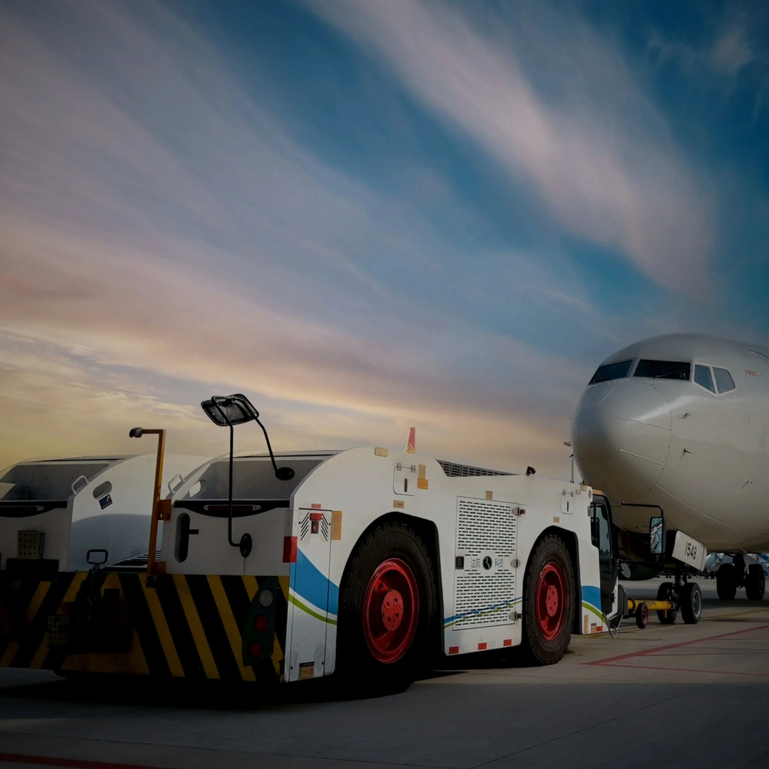 Close-up view of an airplane being towed by a ground vehicle at the airport during sunset.