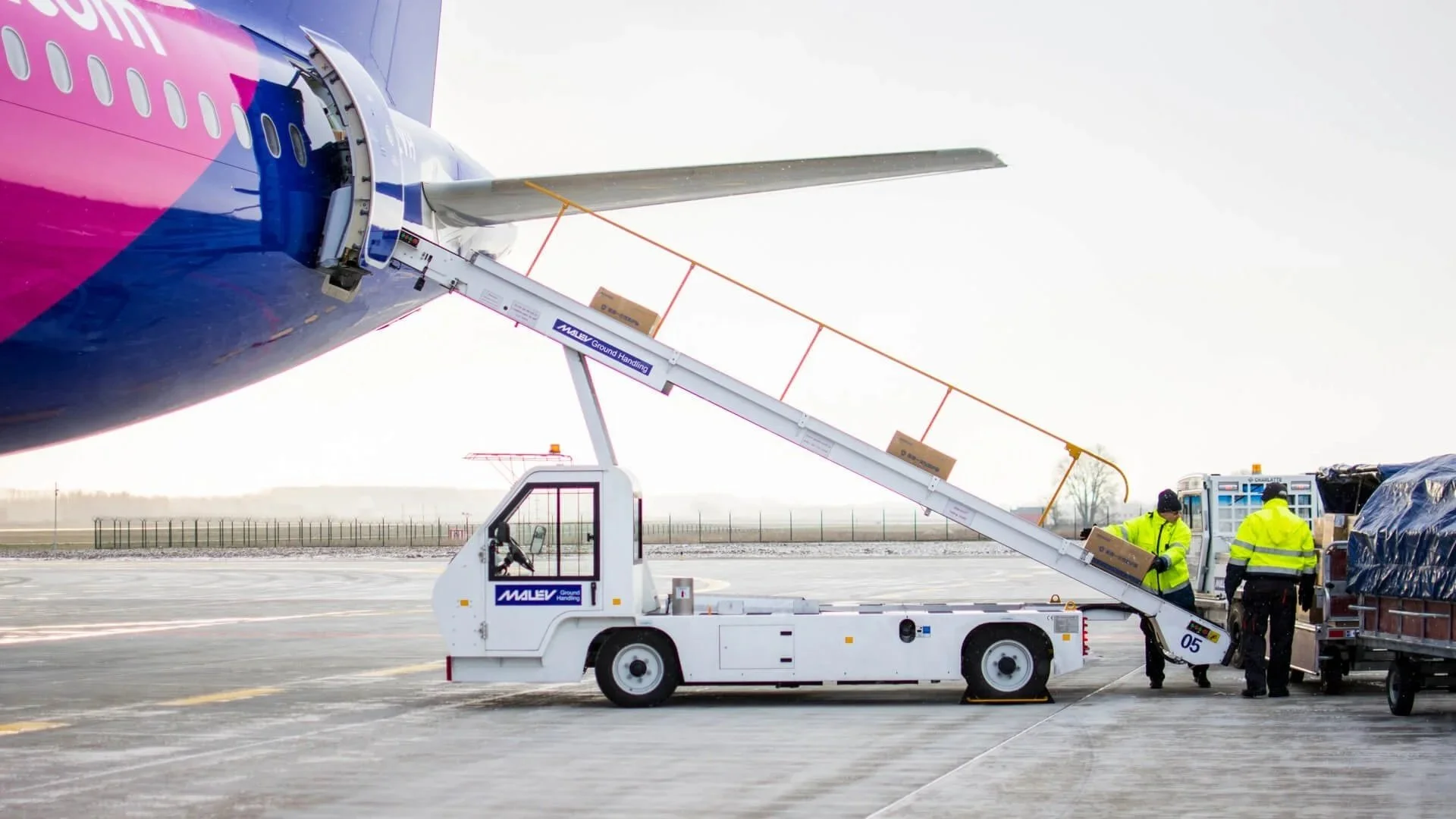 Ground crew loading cargo into an airplane at an airport, with ground handling equipment and personnel in high-visibility jackets.
