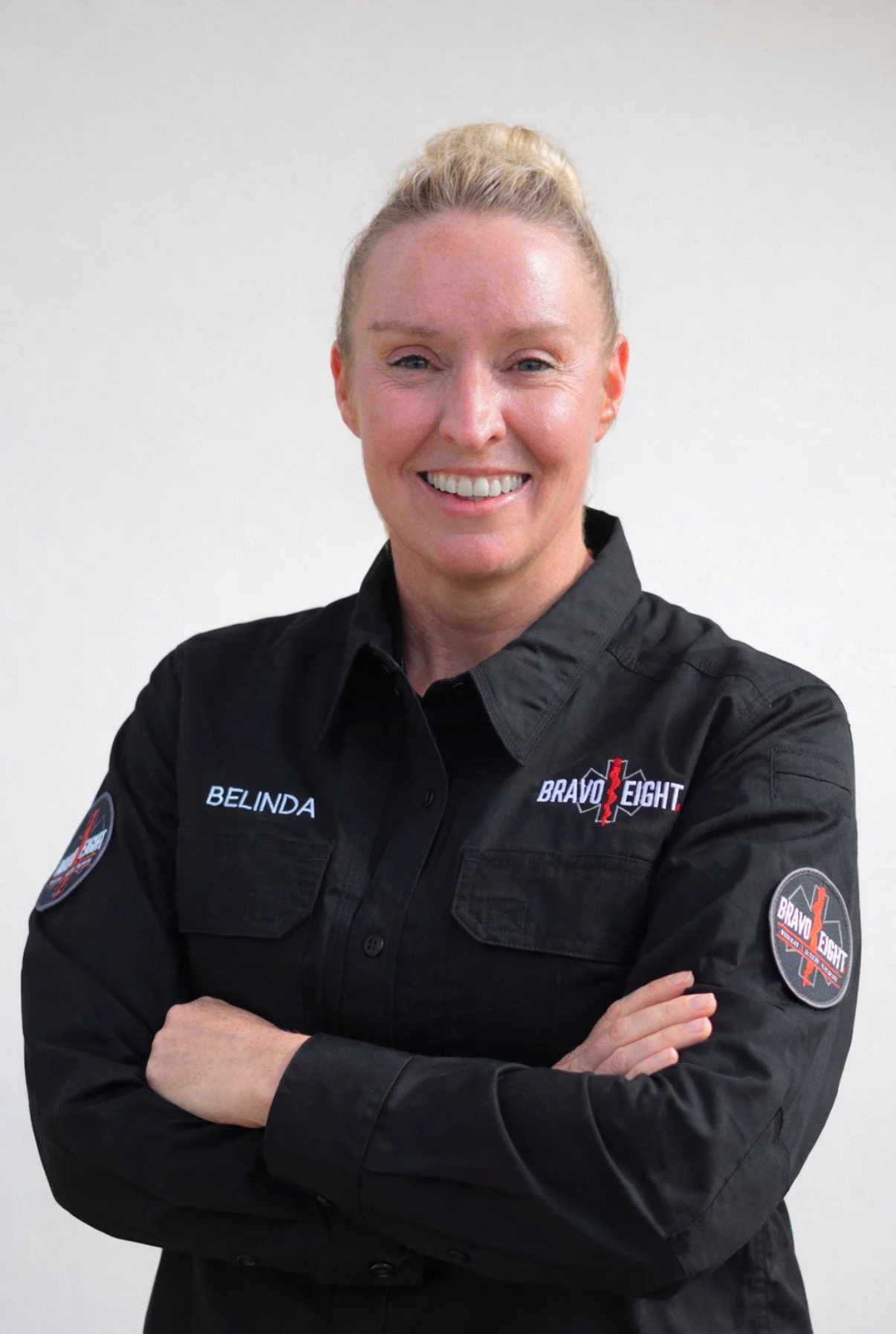 A woman in a black Bravo Eight uniform with her arms crossed, smiling at the camera.