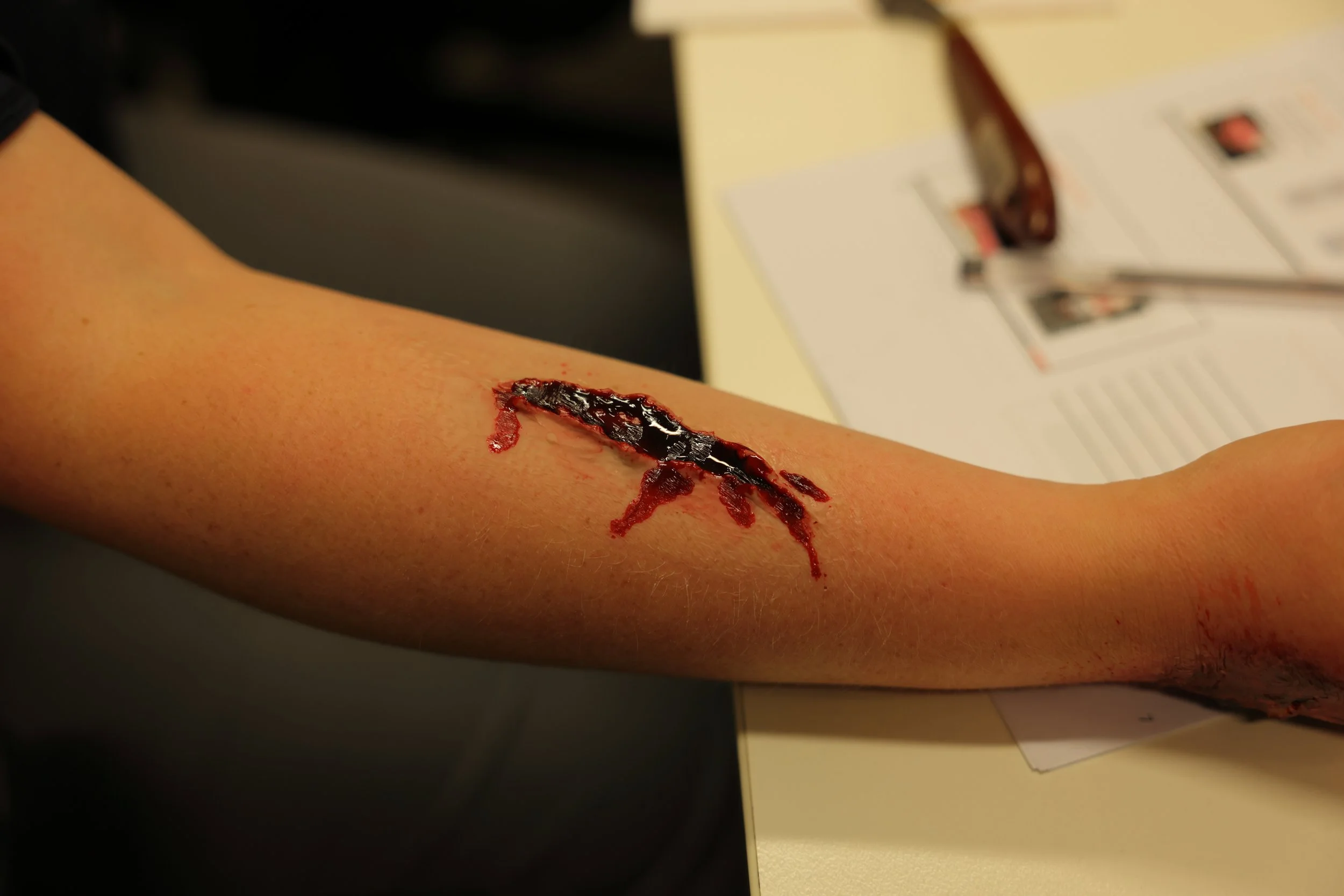 Fake arm with a large, simulated deep laceration showing exposed tissue and bleeding.