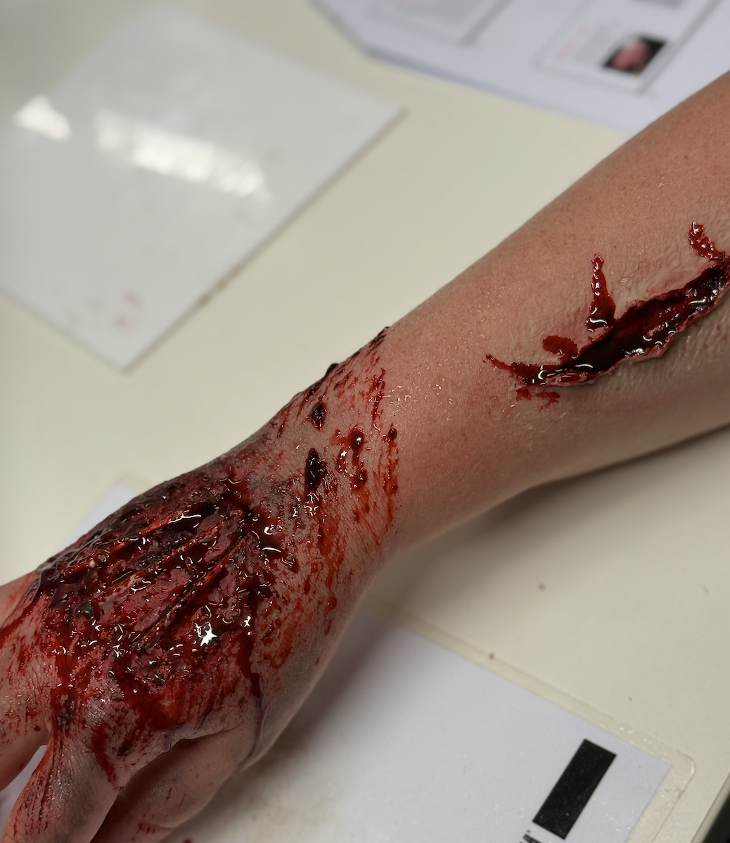 A realistic medical simulation of a severe forearm injury with deep lacerations and bleeding, likely a mannequin or training simulator used for medical training.