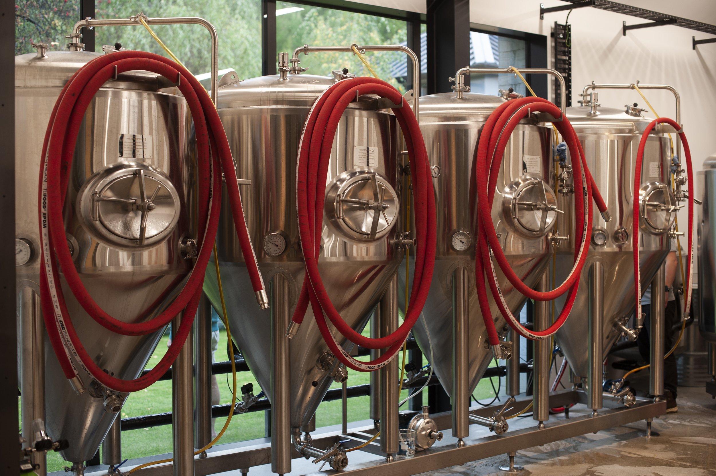 Four stainless steel fermentation tanks with red hoses attached.