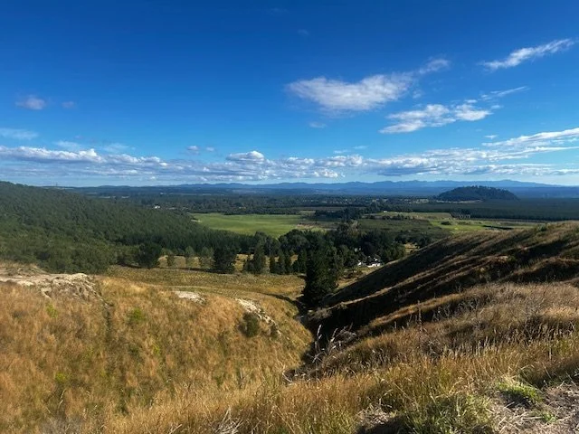 Scenic view of rolling hills, green fields, and a distant mountain range under a partly cloudy blue sky.