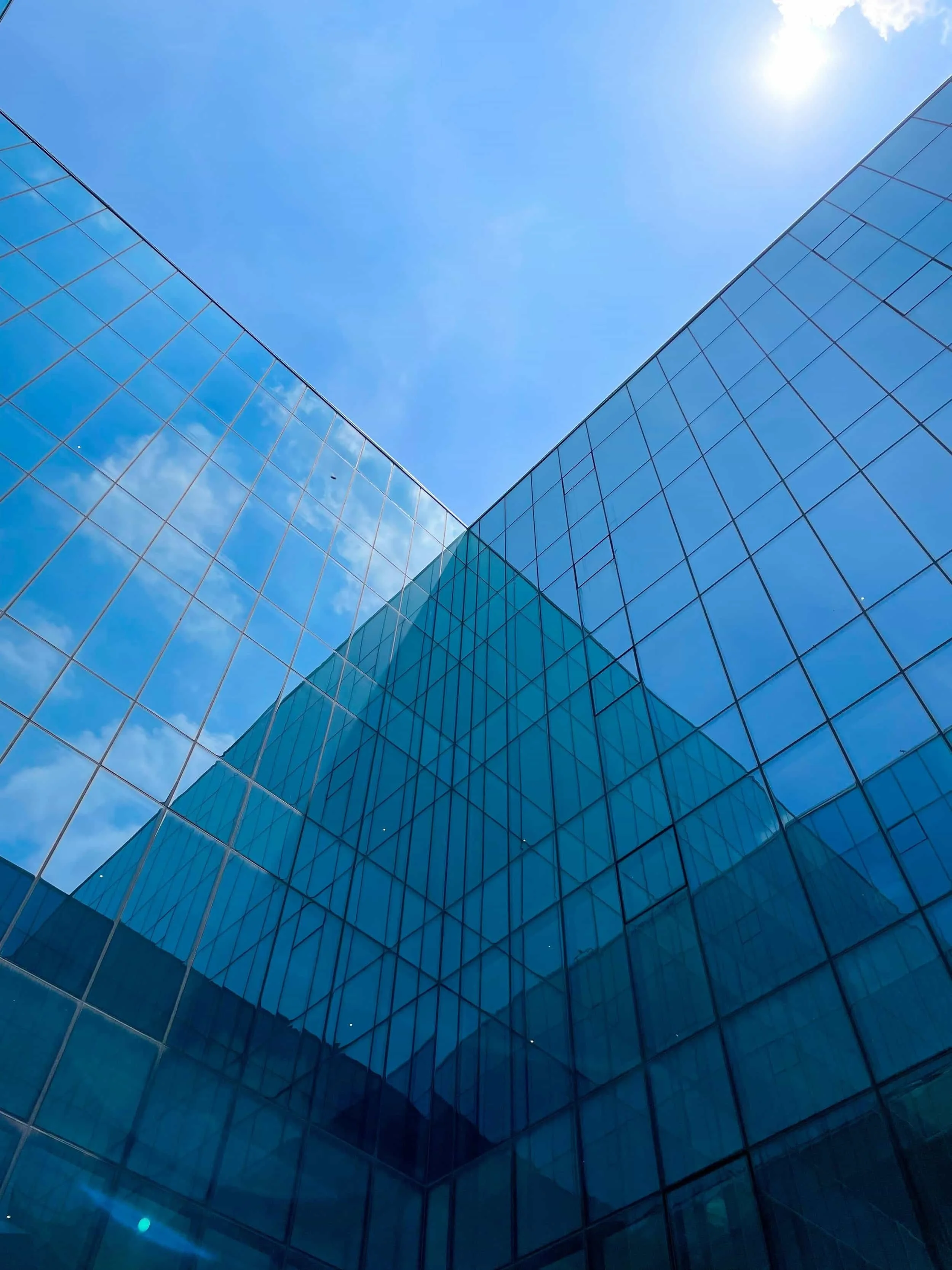 Looking up at a modern, blue glass commercial office building against a clear sky.