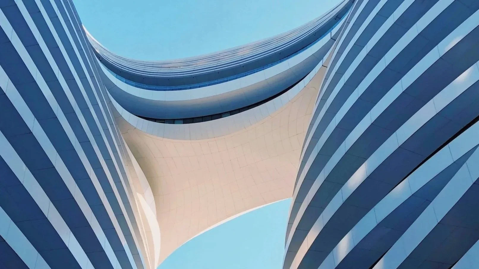Looking up at the sweeping, curved architecture of a modern commercial property against a clear blue sky.