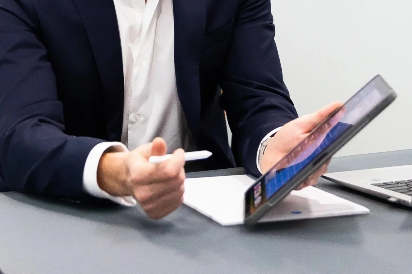 Close-up of a professional in a suit holding a digital tablet and stylus, representing contract signing and vendor certainty.