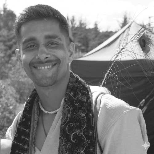 A young man smiling outdoors in front of a tent with trees in the background.