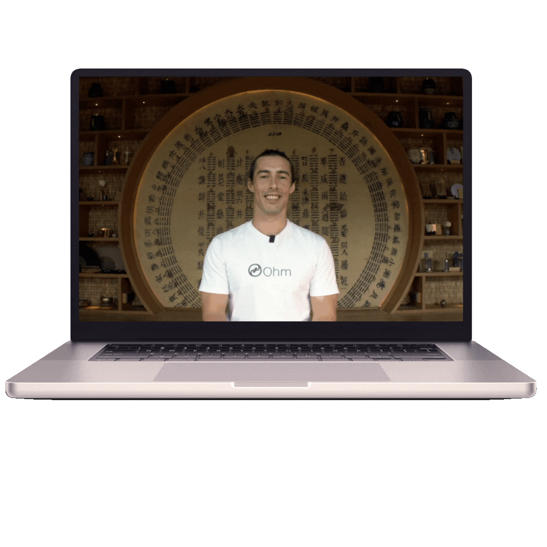Laptop displaying a man with dark hair in a white T-shirt smiling, with a background of traditional Balinese shelves and calligraphy.