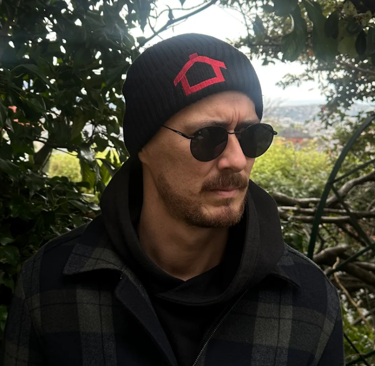 A man wearing a beanie in front of a paddock. 