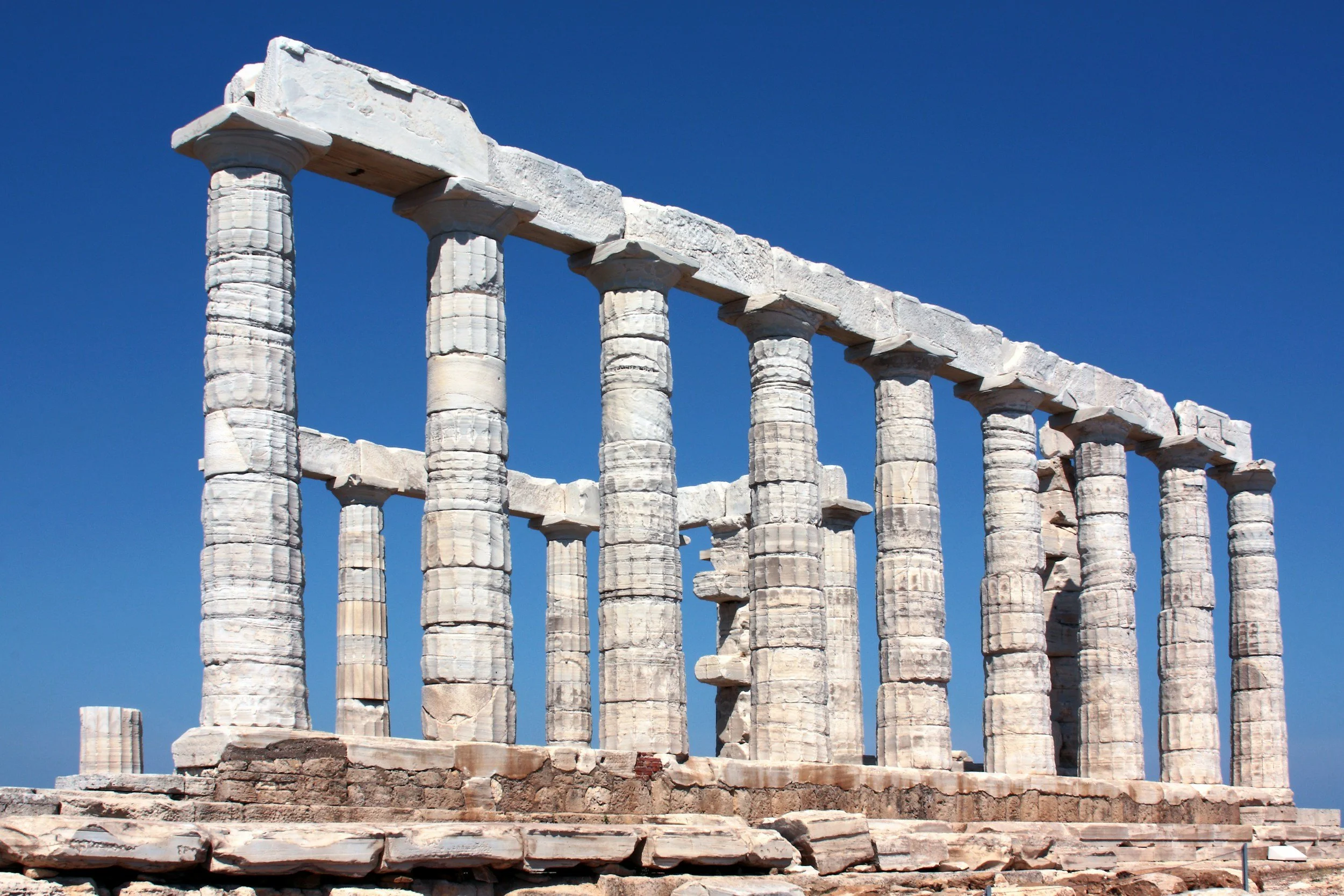 Ancient Greek temple ruins with tall white marble columns against a clear blue sky.