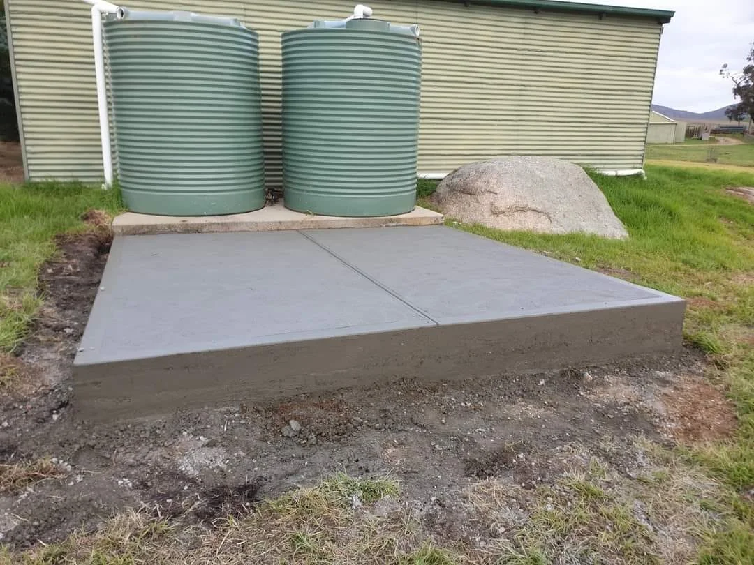 Concrete slab next to two green water tanks outside a building with corrugated metal siding.