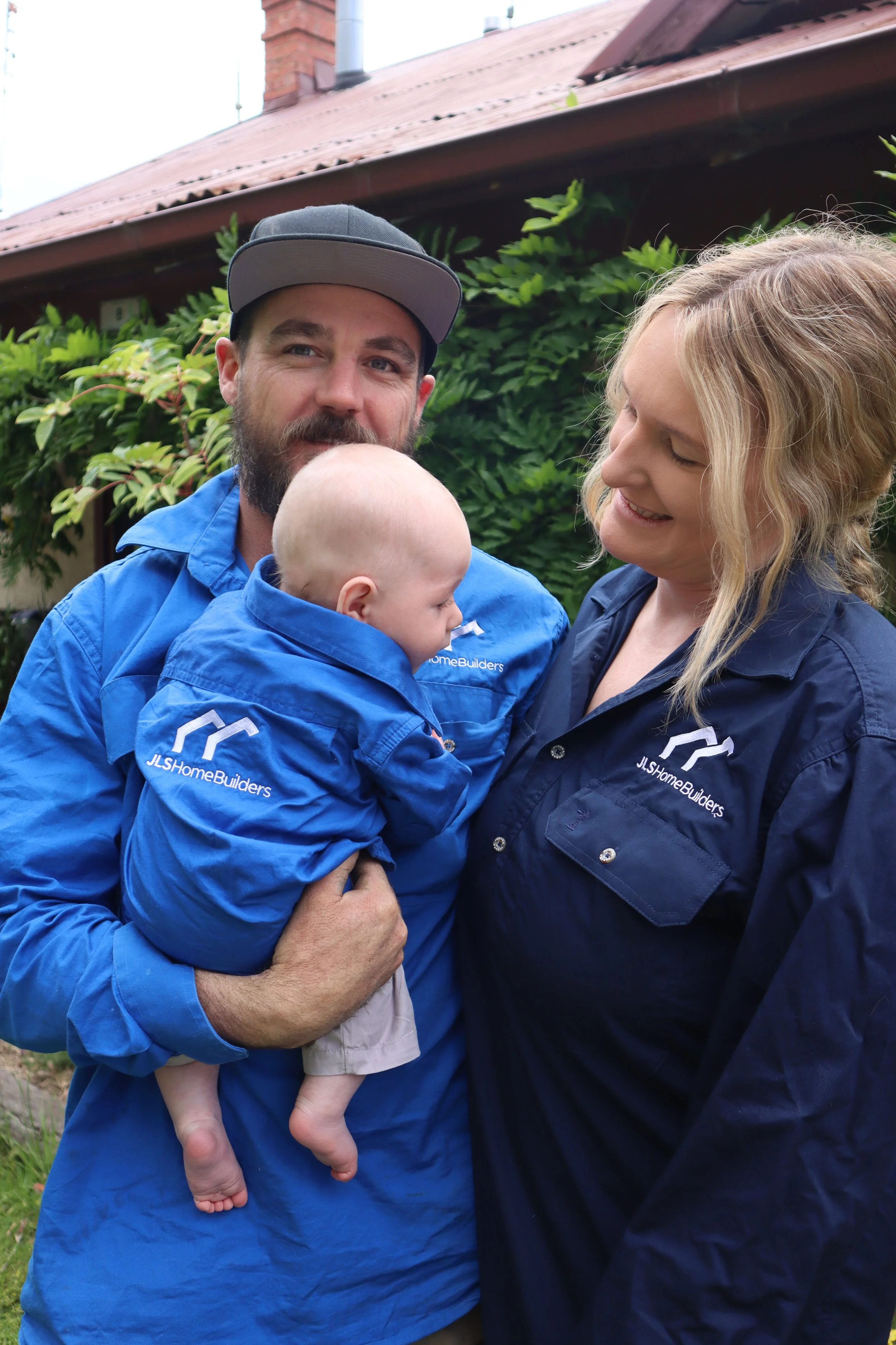 Jack and Family in front of home smiling, wearing JLS home Builders branded shirts.
