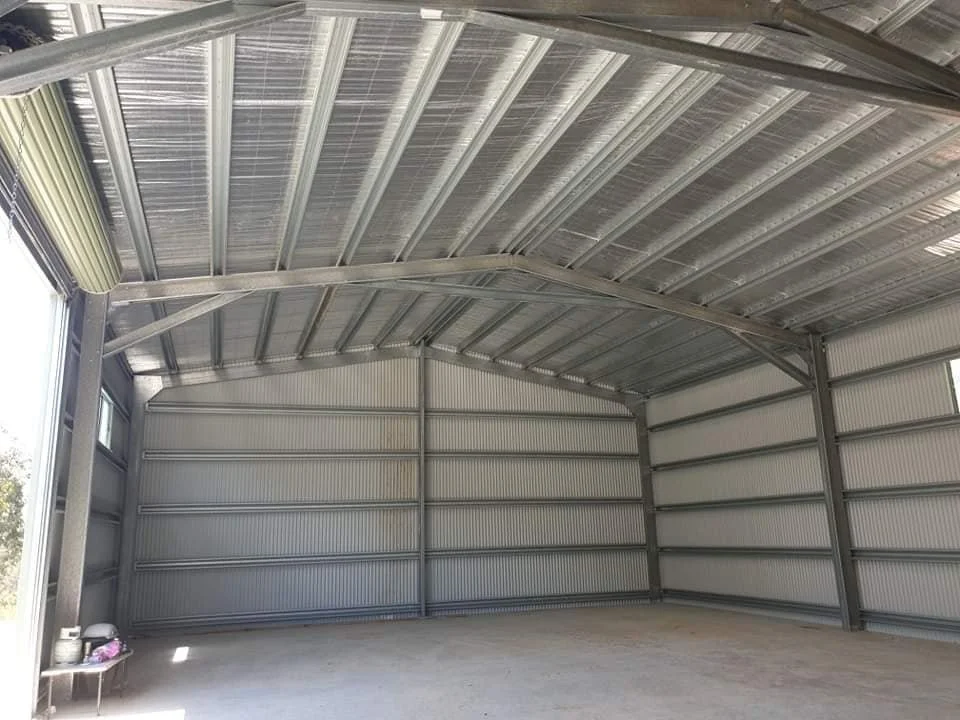 Empty metal storage or garage building with reinforced steel walls and roof, concrete floor, and a small table with objects on it in the corner.