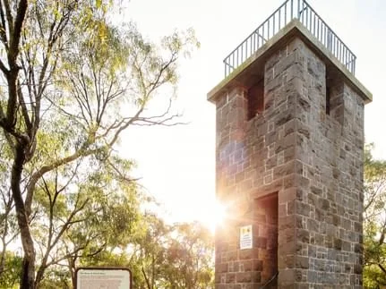 Stone observation tower located in Kilmore Victoria with a railing on top, set among trees with sunlight peeking through.