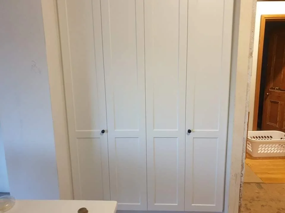 A white closet with four doors and black knobs in a room with beige walls.