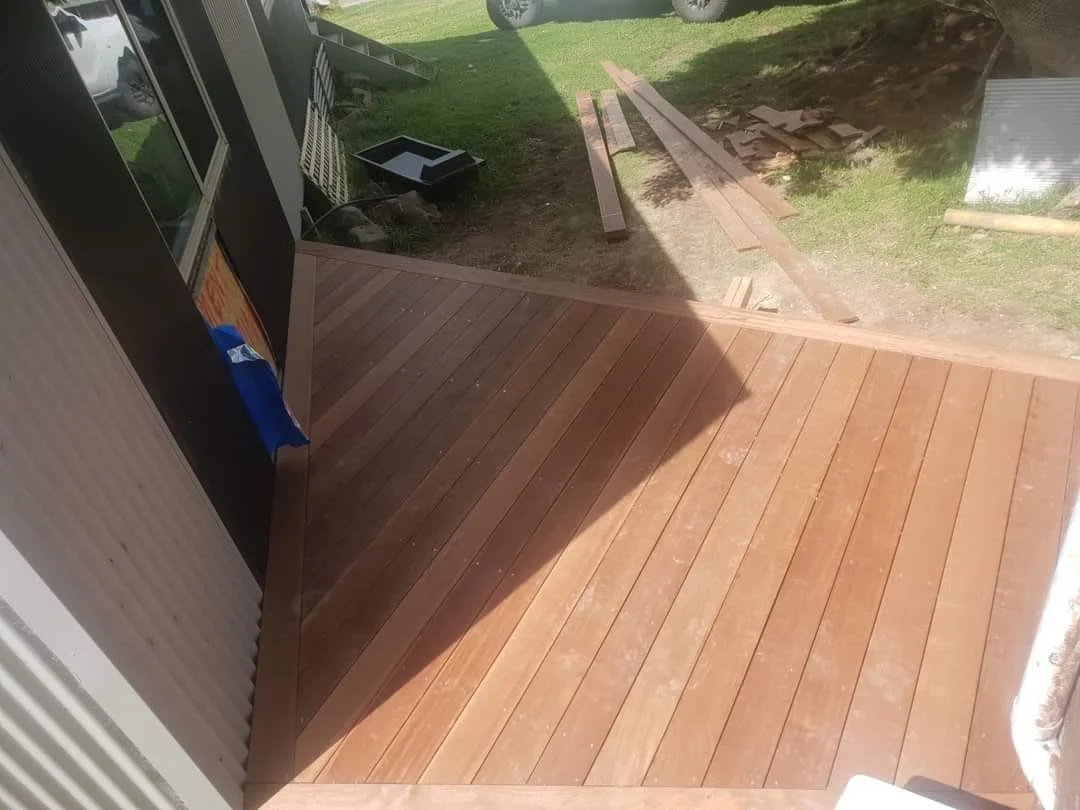 Newly installed wooden deck patio with tools and materials nearby, outside a house with grass and a vehicle in the background.