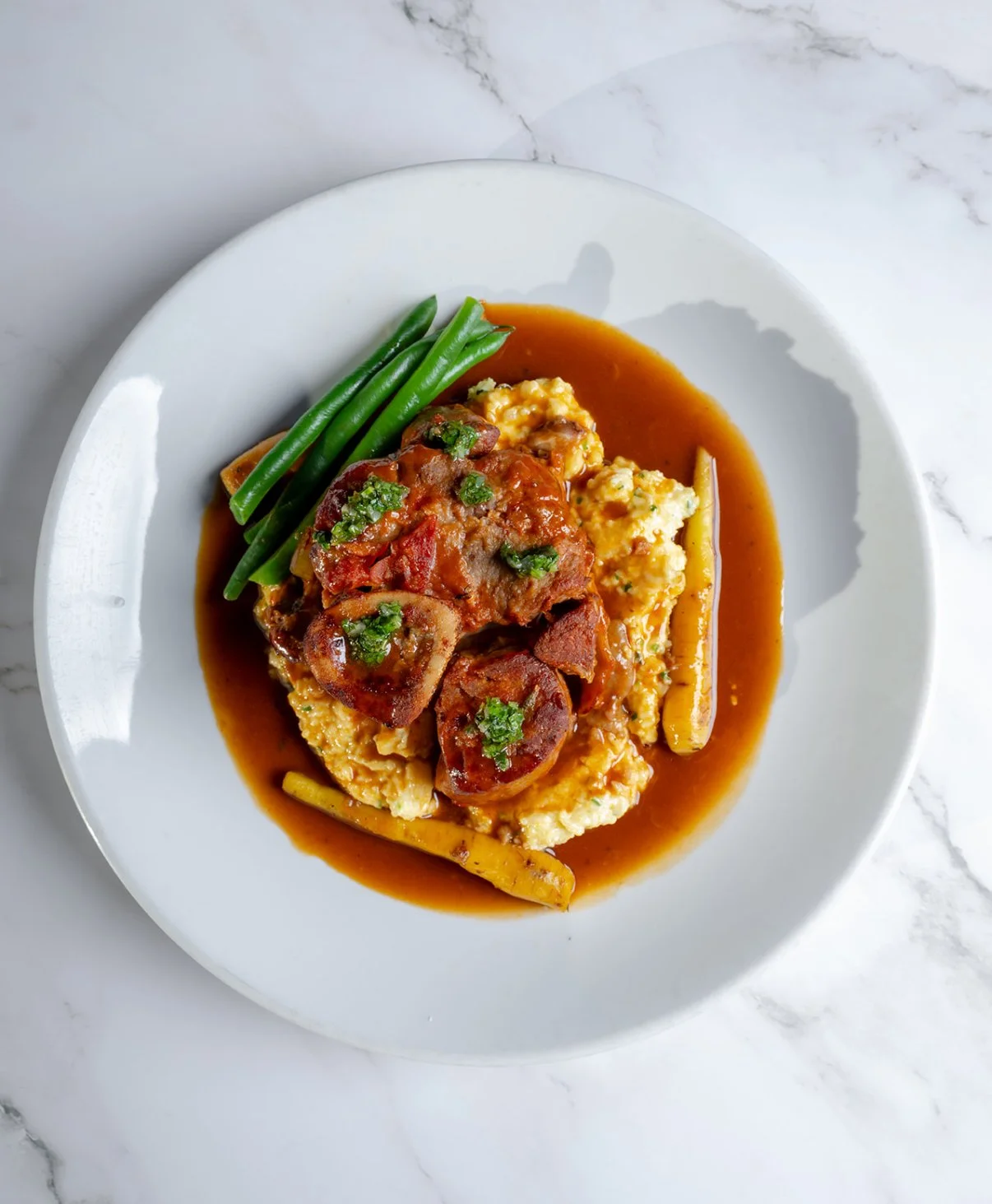 Plate of mashed potatoes topped with meatloaf and gravy, green beans on the side.