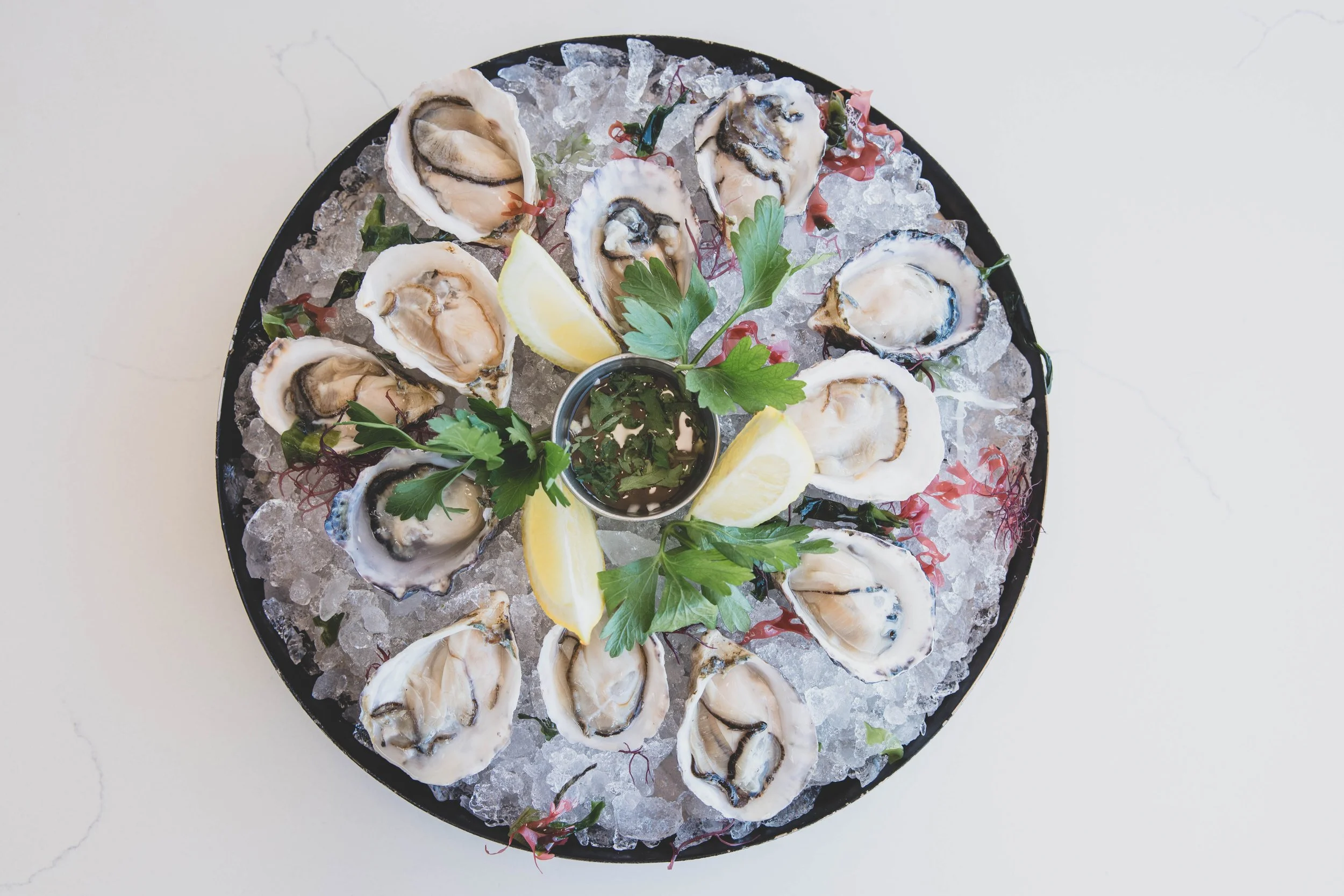 Plate of raw oysters on ice garnished with lemon wedges, parsley, and sauce
