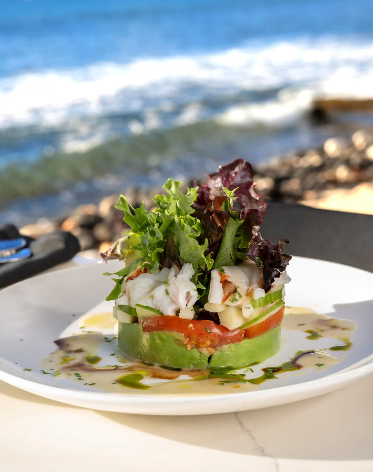 Seafood salad on a white plate with pineapple, tomato, cucumber, lettuce, and dressing, on a table at the beach.