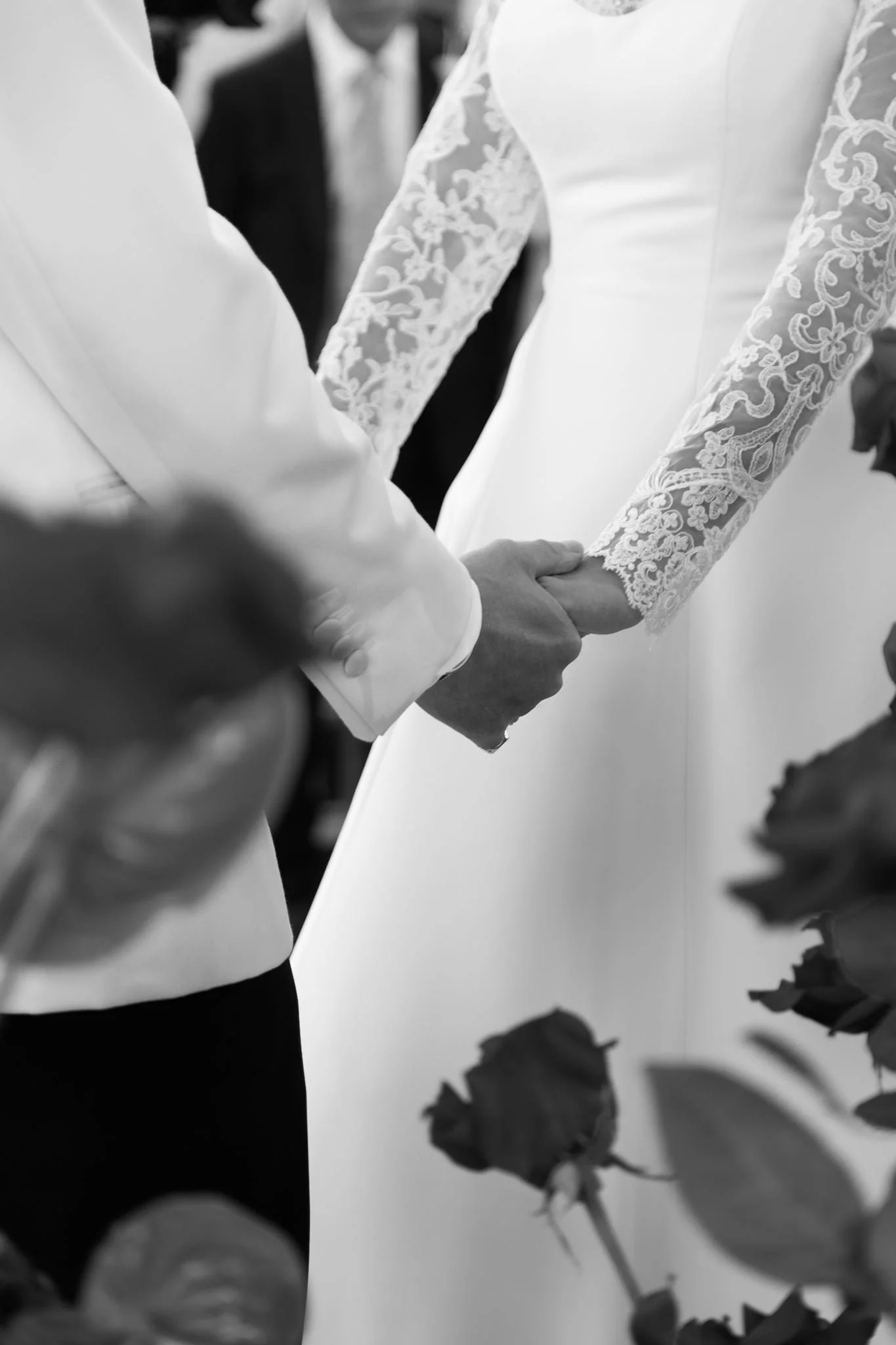 A couple holding hands, dressed in wedding attire, during a wedding ceremony or celebration.
