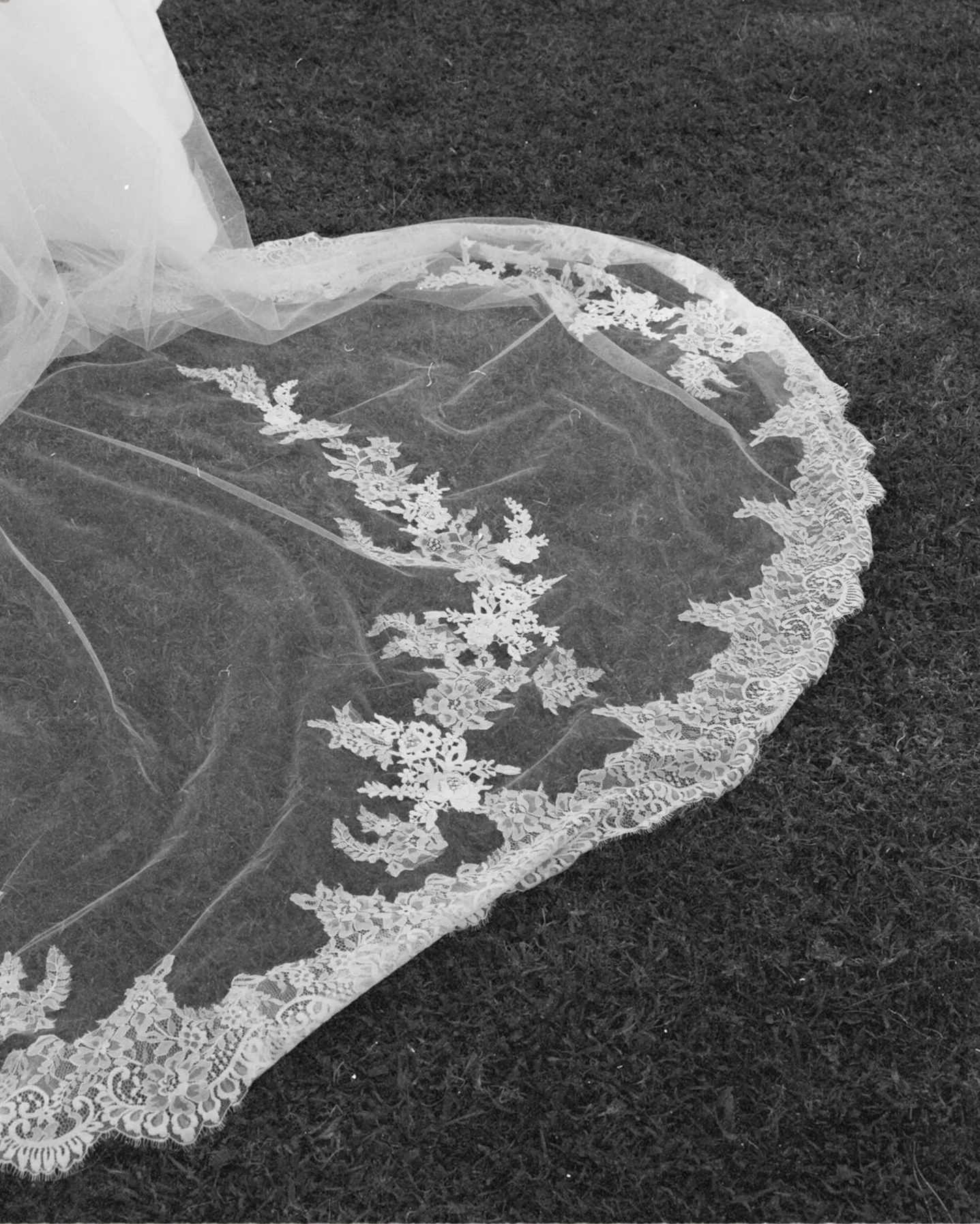 A delicate lace veil with floral embroidery lies on a grassy surface.