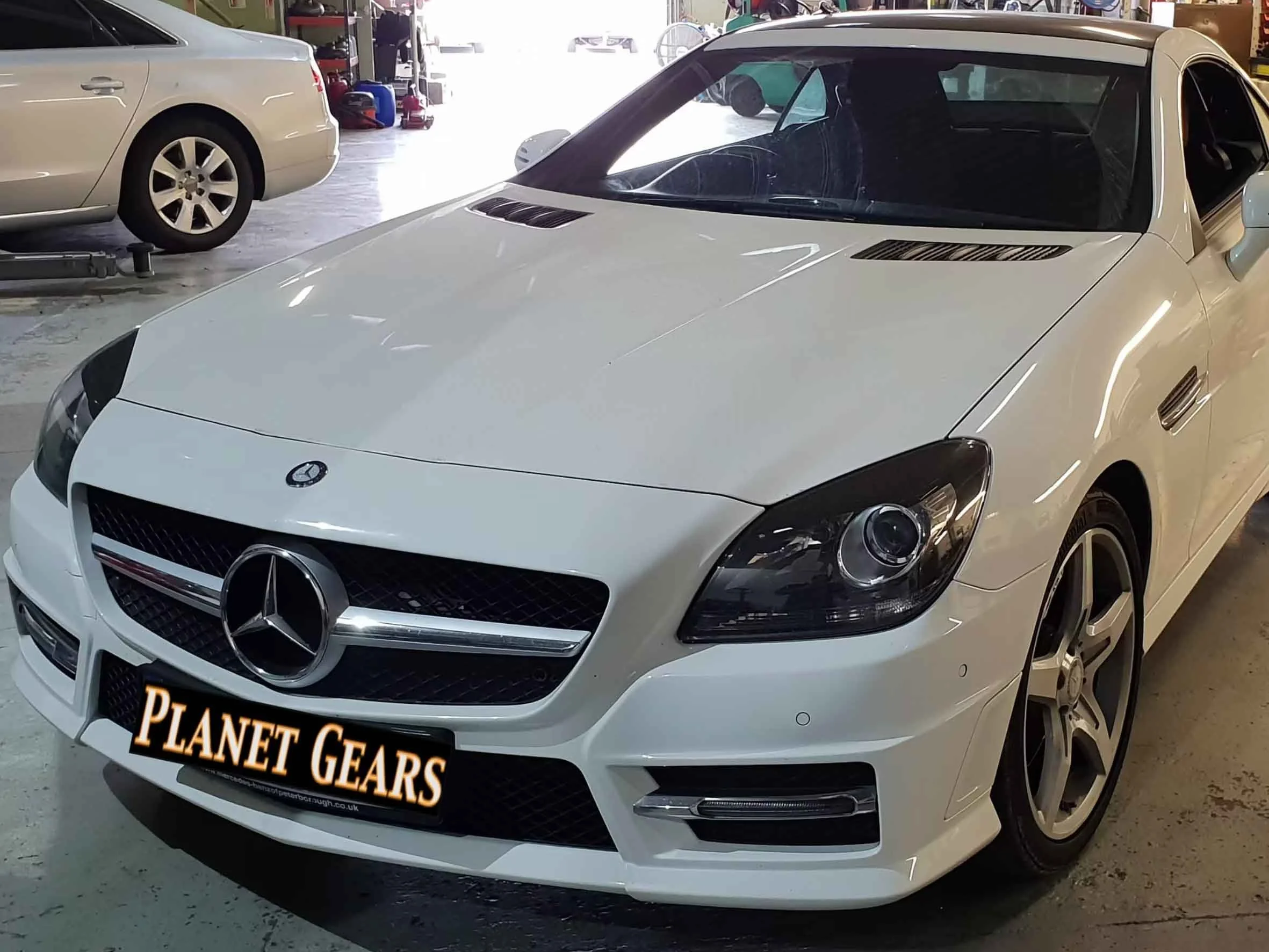 A white Mercedes-Benz sports car parked inside a garage with another silver car visible in the background.
