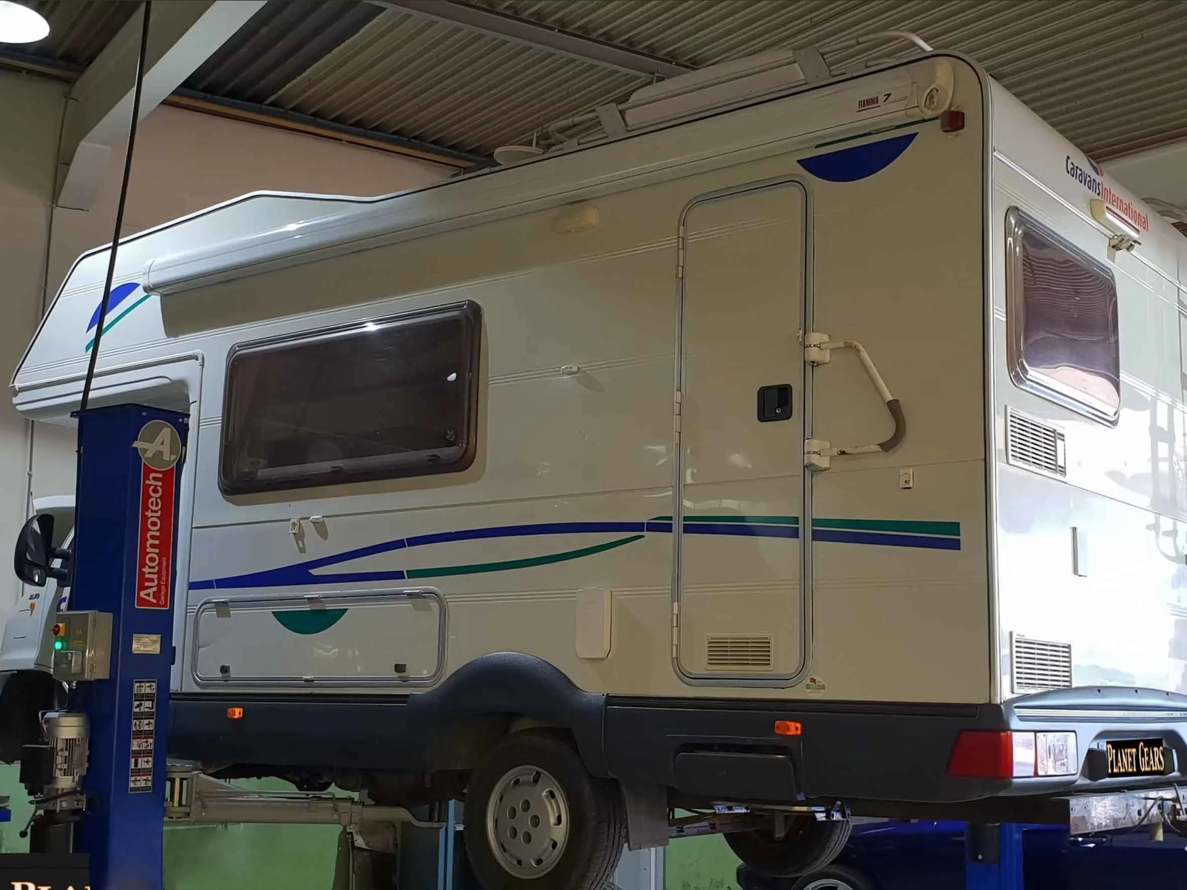 A white caravan on a blue vehicle lift inside a garage.