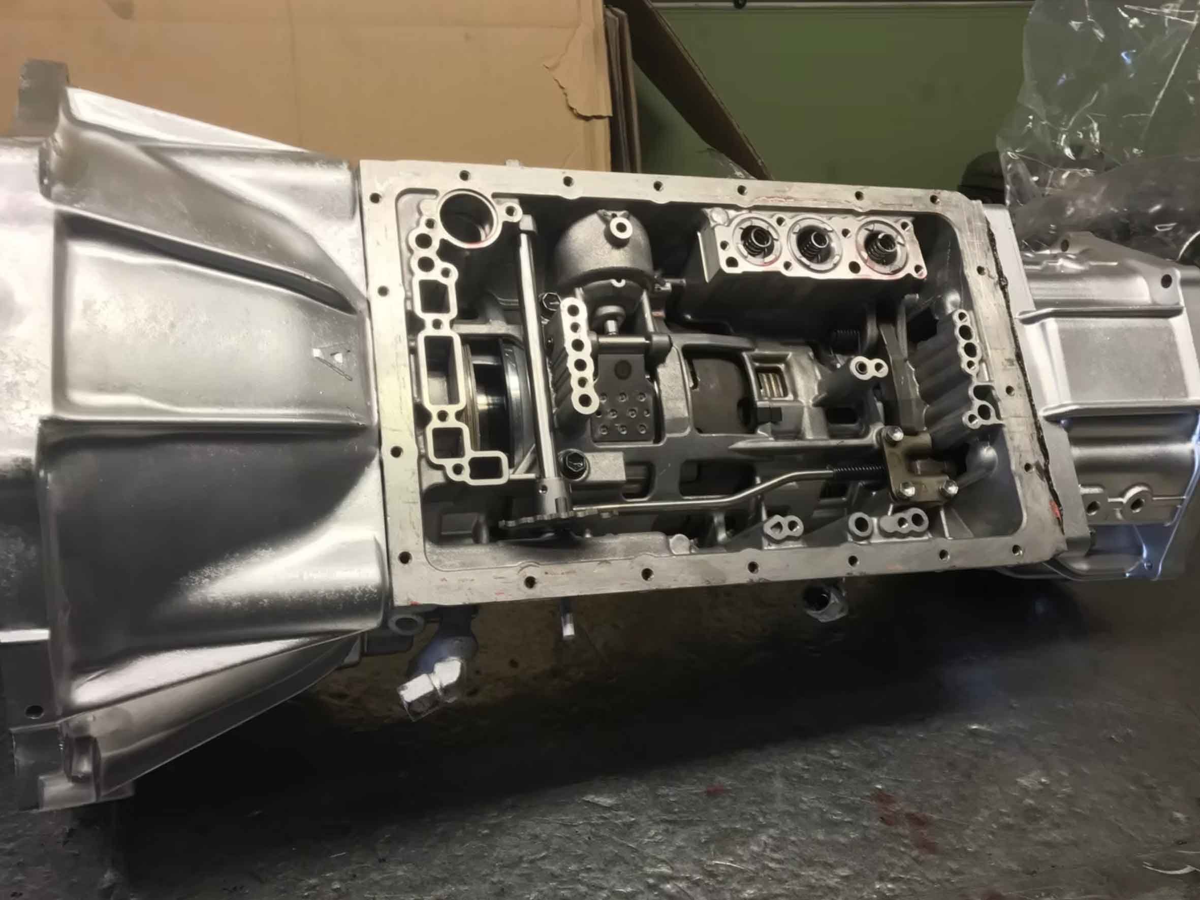 An exposed automotive transmission with visible internal components, mounted on a workbench in a workshop.