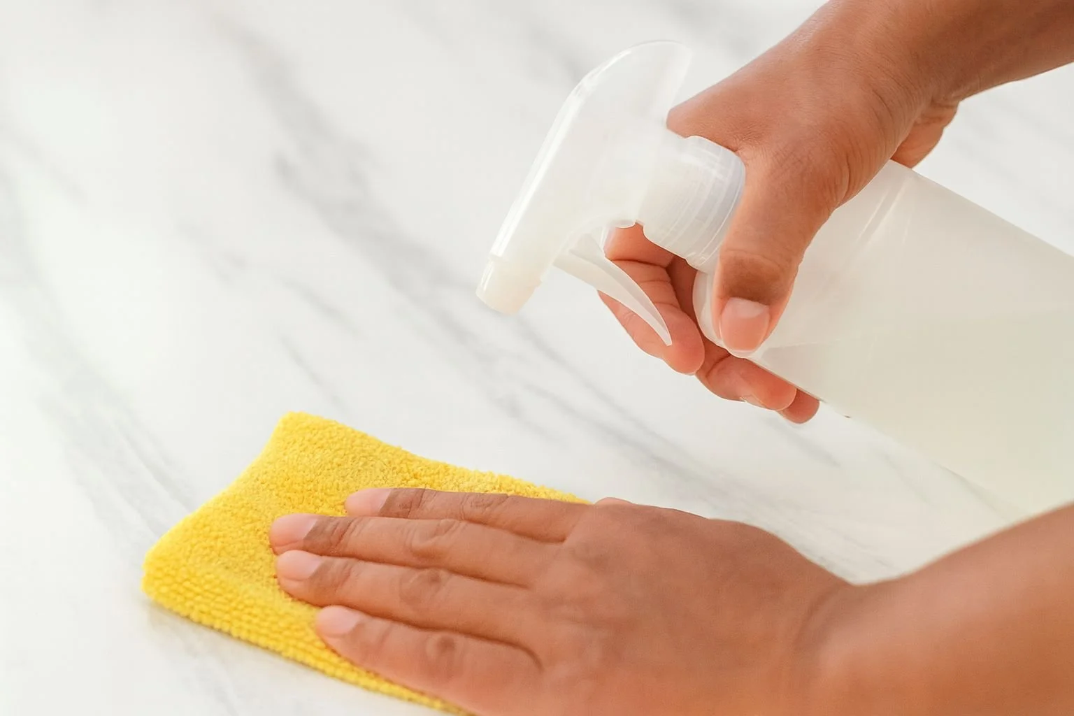 Hand spraying cleaning solution on a yellow microfiber cloth.