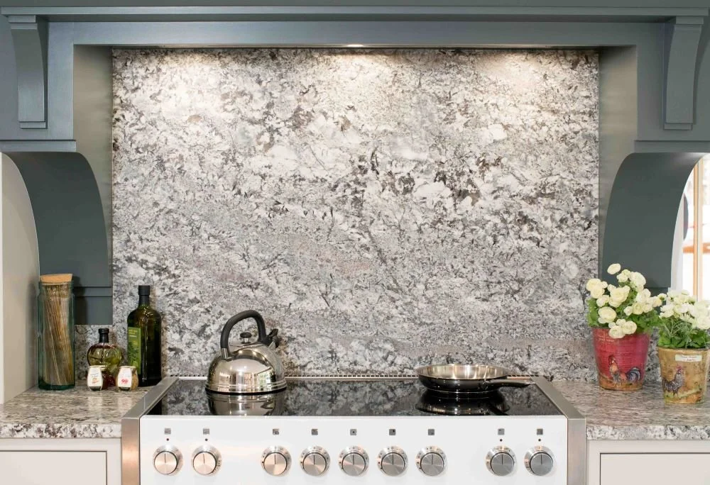 Kitchen stovetop with a kettle, a frying pan, and decorative pots and bottles, featuring a granite backsplash and countertop.
