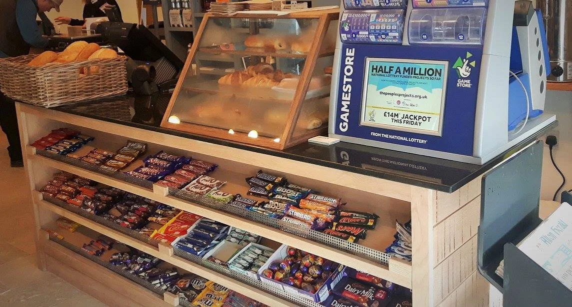 Newly stocked bakery display case with croissants and bread, beside a snack counter with chocolate bars and snacks, and a lottery ticket machine on top.