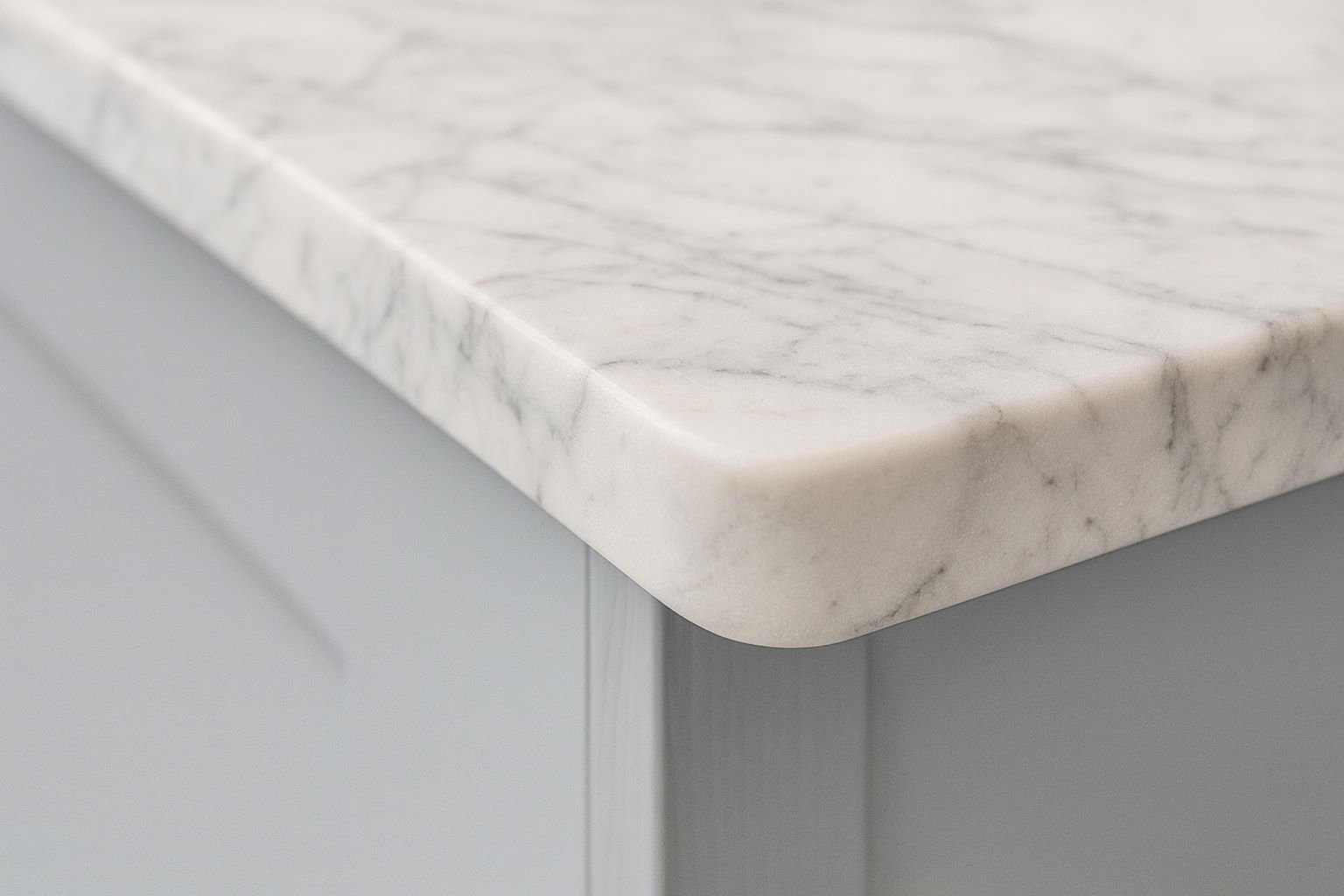 Close-up of a white marble countertop with gray veining, mounted on a white cabinet with a beveled edge.