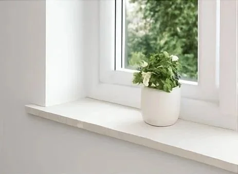 A marble window sill with a potted plant with white flowers outside a window.