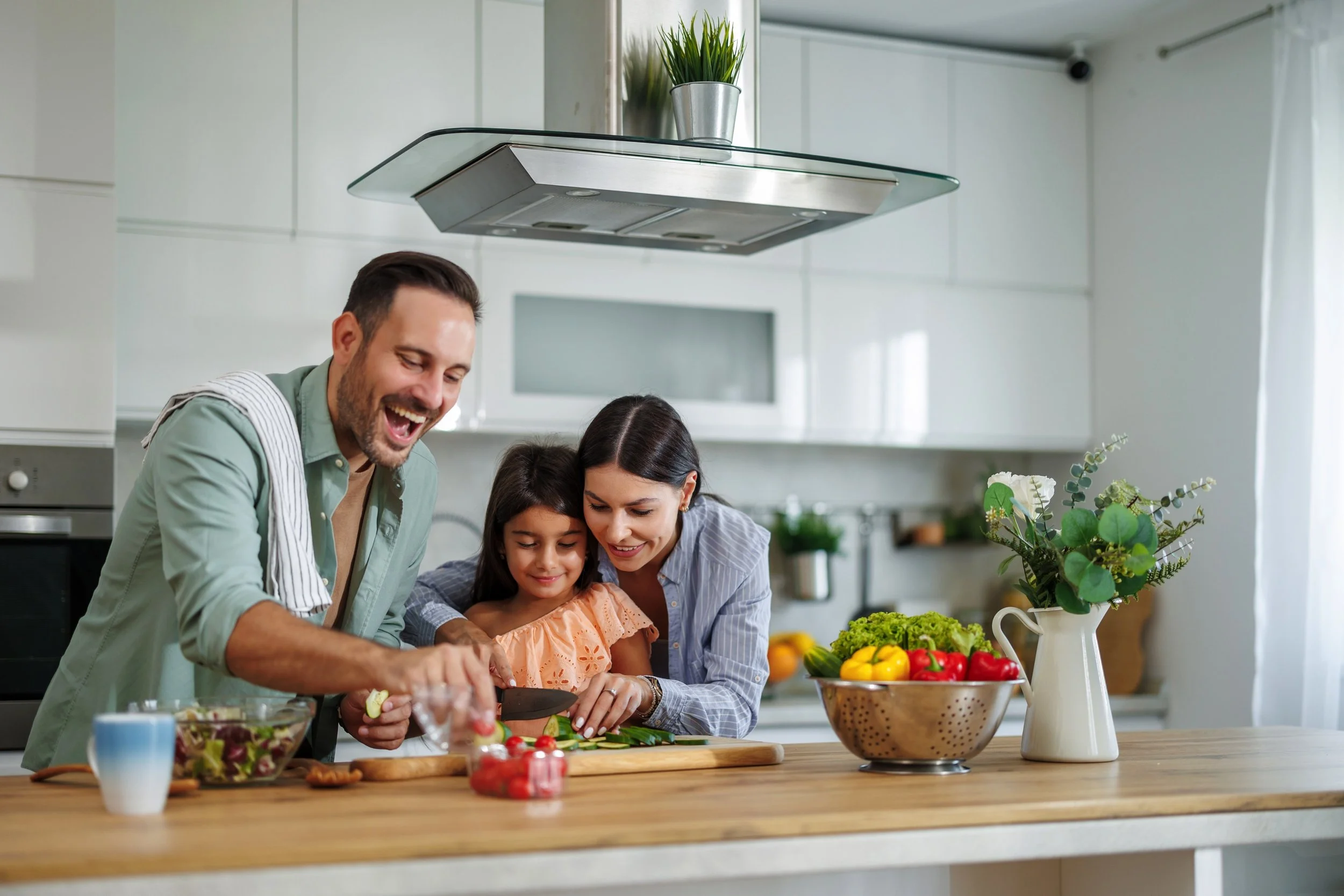 Family cooking together in a modern kitchen with fresh vegetables on the counter.