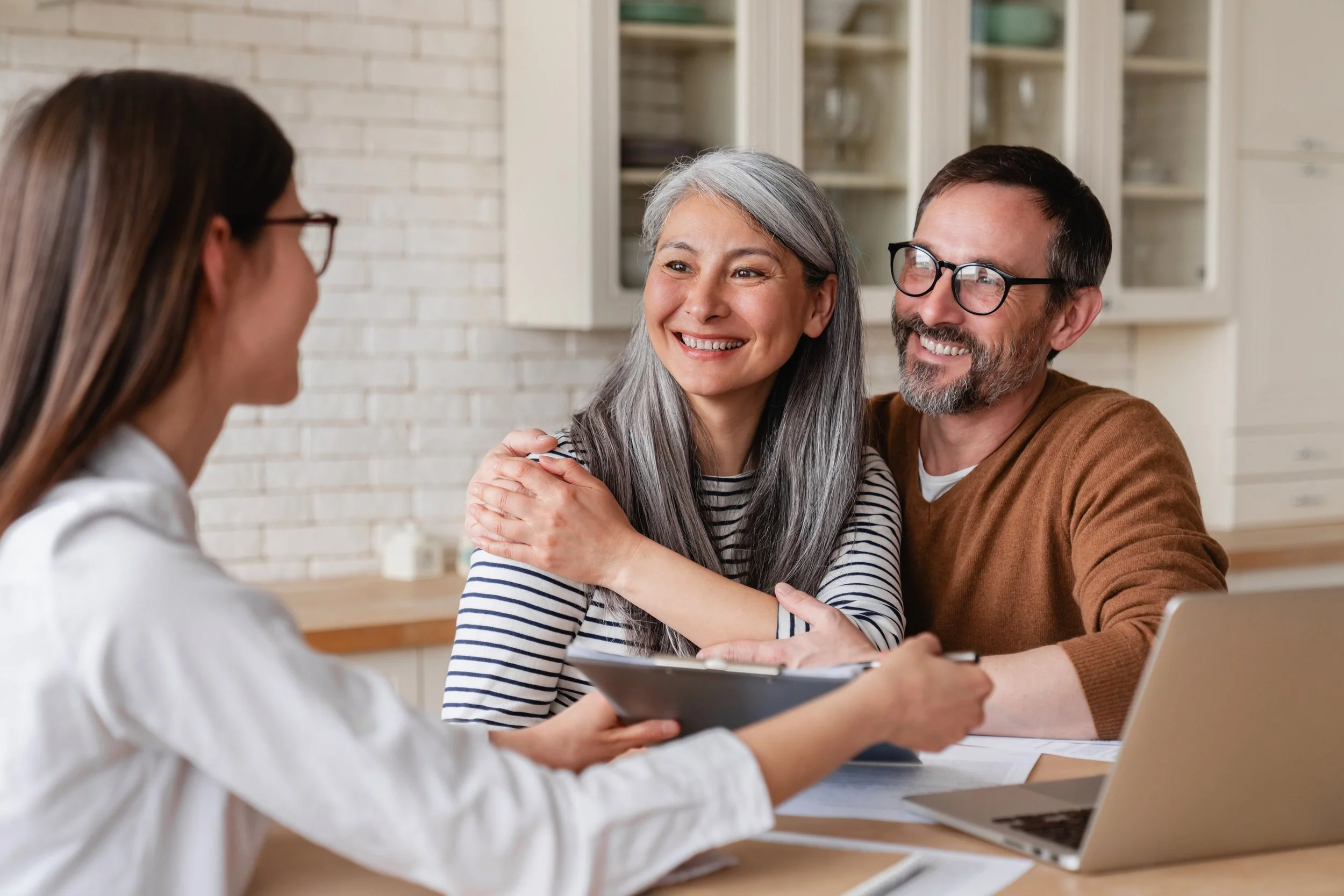 A happy couple meeting with a woman in an office or consultation setting, smiling and listening attentively.
