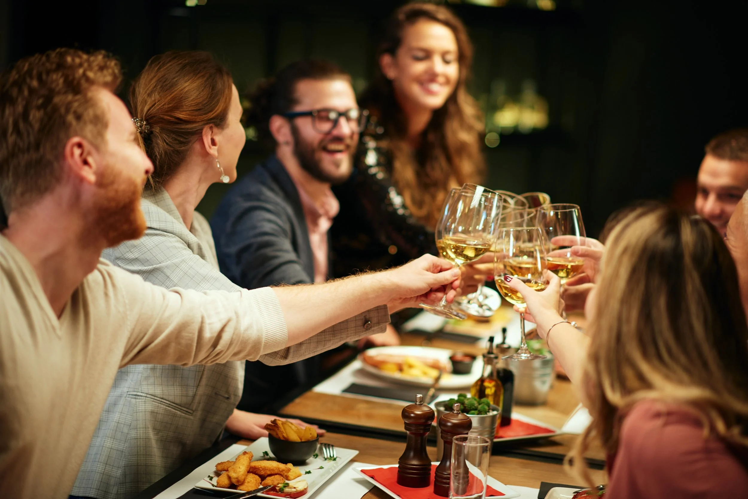 Group of friends raising wine glasses for a toast at a dinner table.