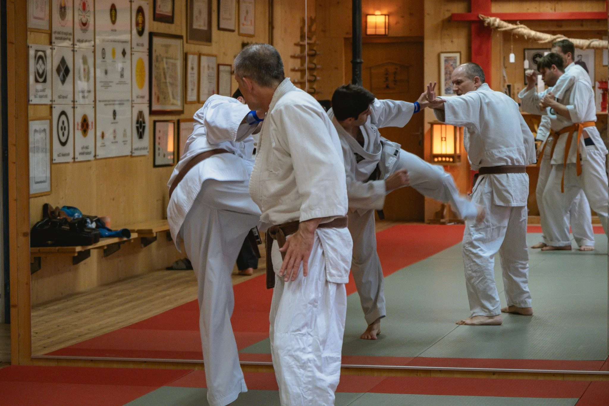Menschen im Dōgi beim Training in einem authentischen Dojo, die Wand mit Preis- und Urkundenanzeigen im Hintergrund.