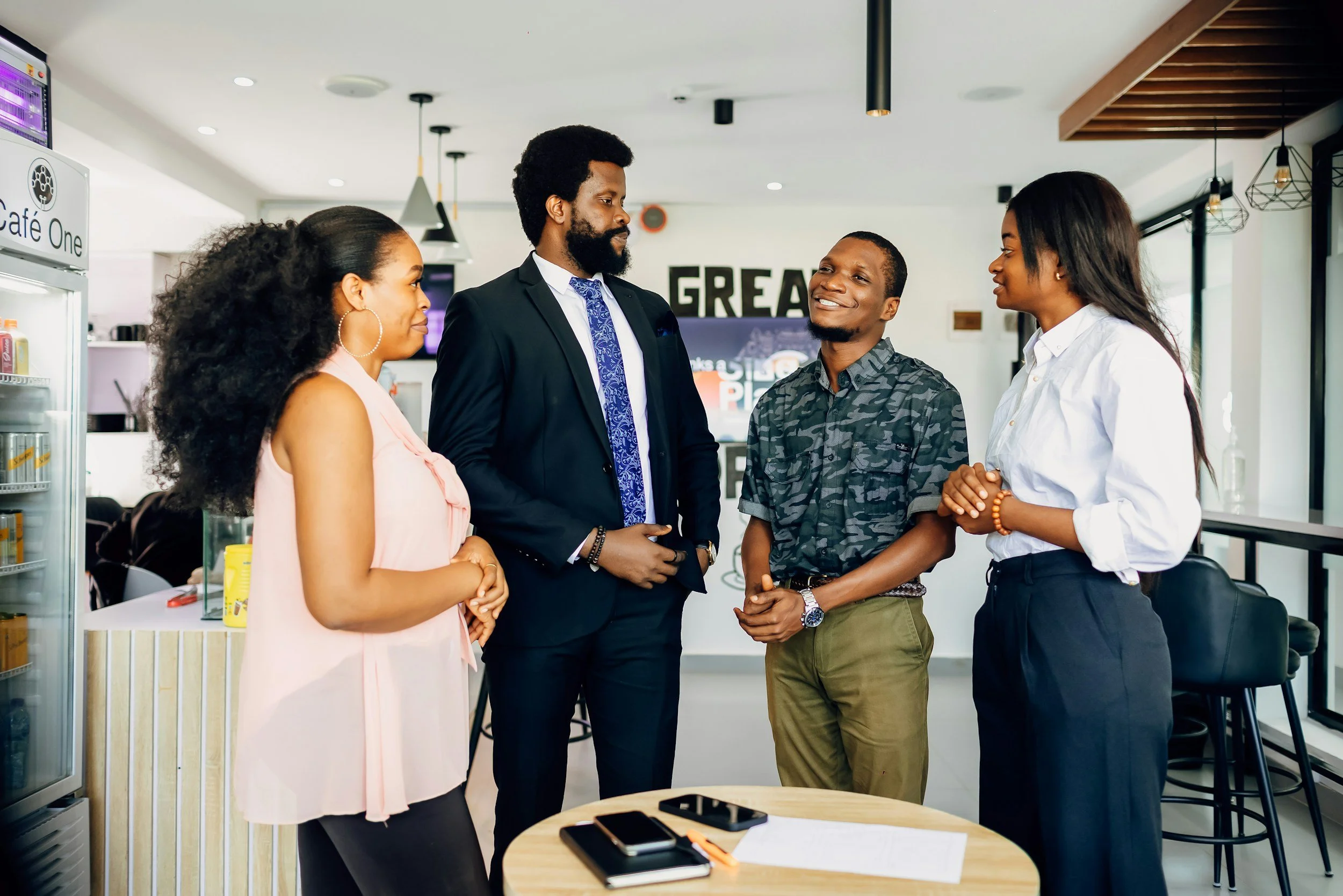 Five people having a conversation in a modern cafe or office space, smiling and engaging with each other.