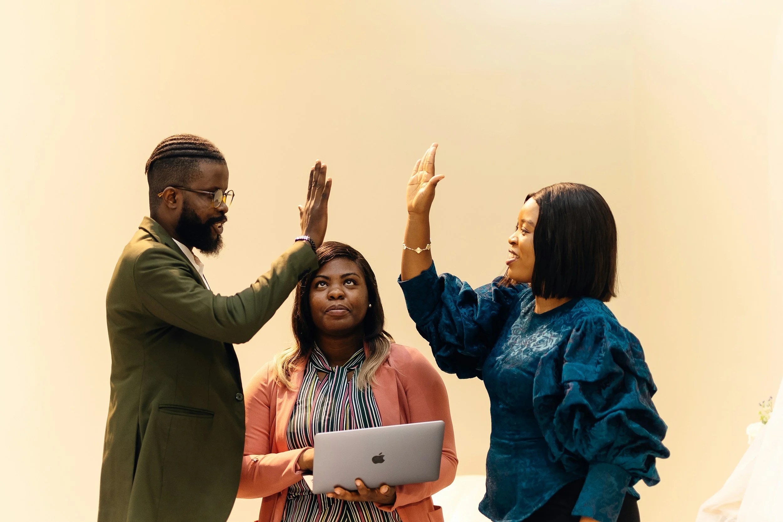 Three people giving each other a high five at an indoor event, with one woman holding a laptop.