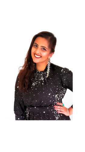 A woman with long dark hair, wearing a black dress with white speckles and shiny embellishments, smiling and posing with her hand on her hip against a white background.