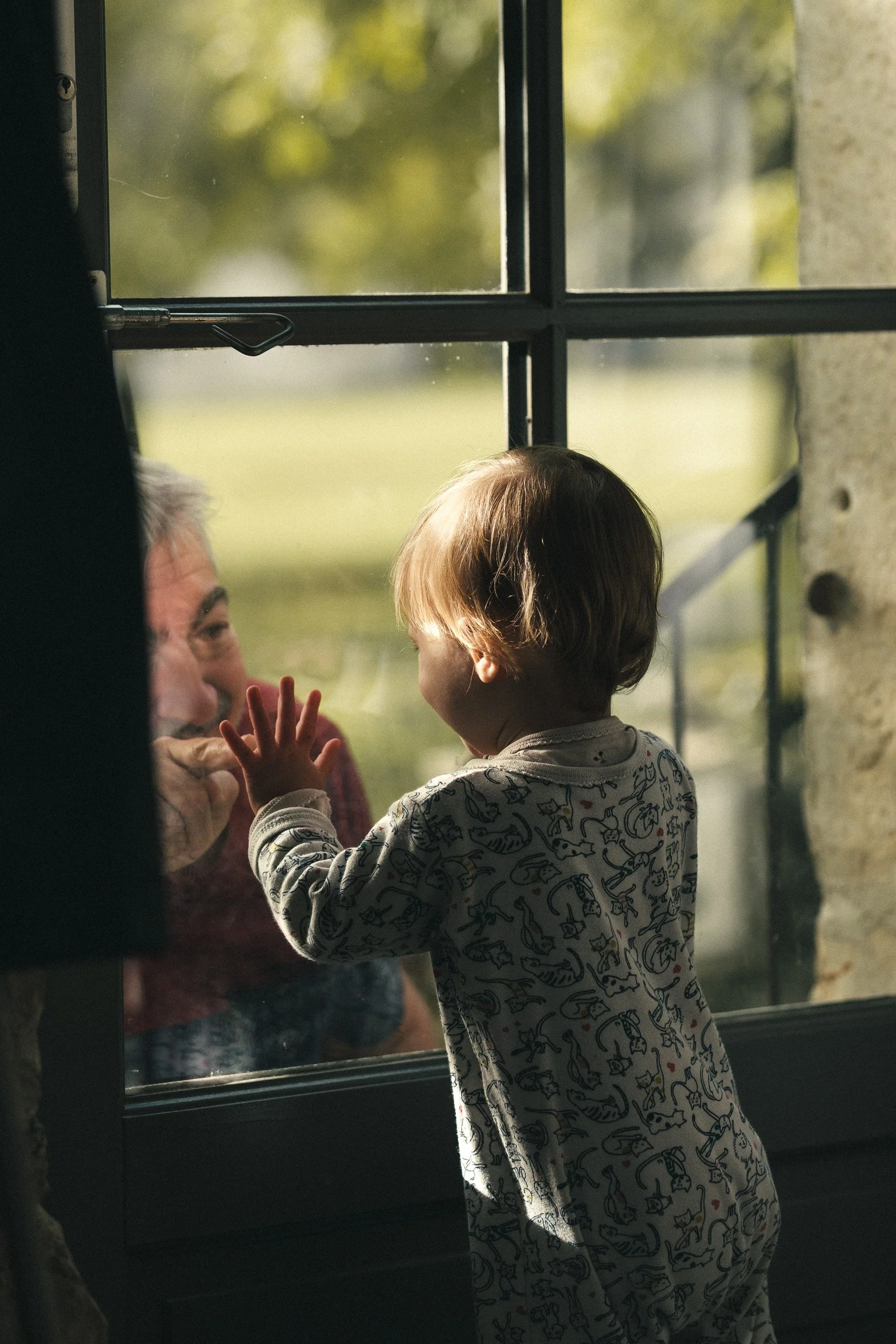 Enfant souriant apercevant son grand-père à travers une vitre, complicité captée sur le vif — Guillaume Auray-Runel photographe famille Caen