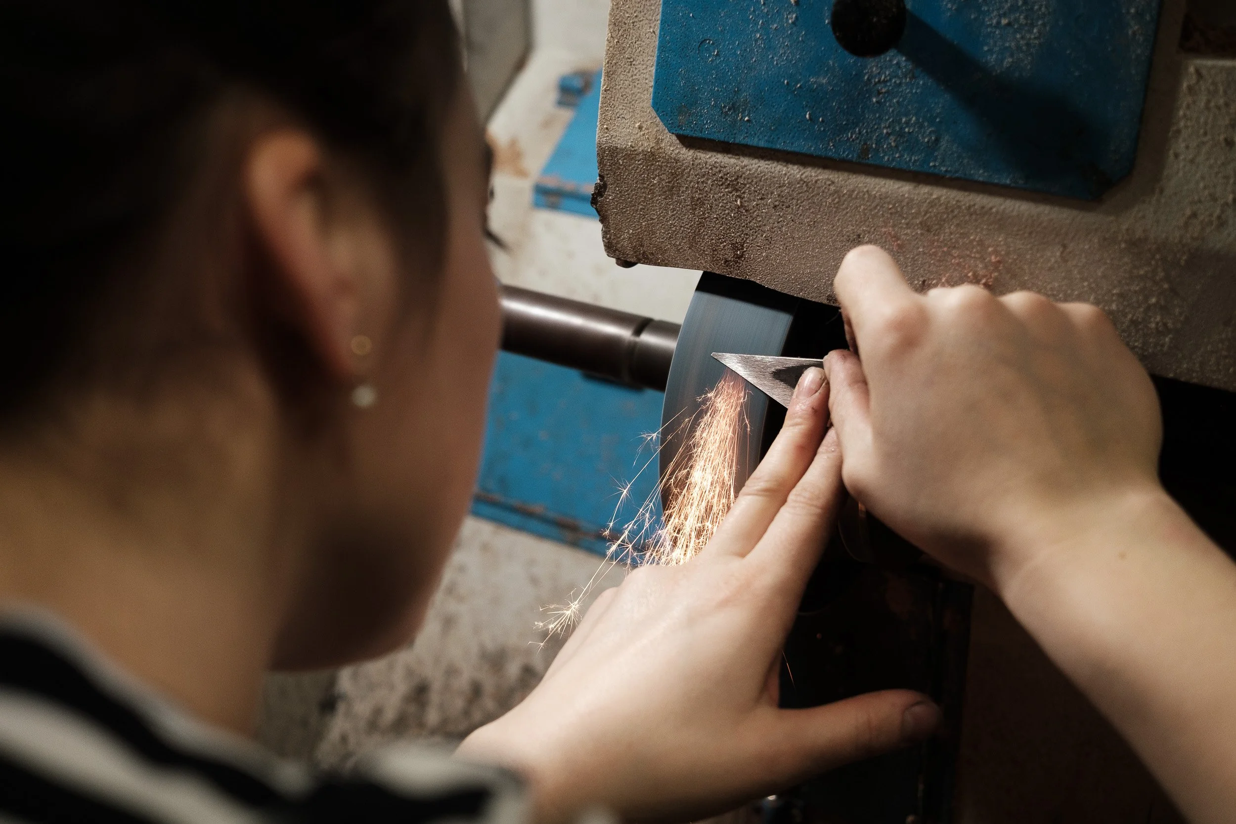 Femme utilisant une meuleuse dans son atelier afin d’aiguiser un outil, scène de travail captée sur le vif — Guillaume Auray-Runel photographe reportage métier Caen