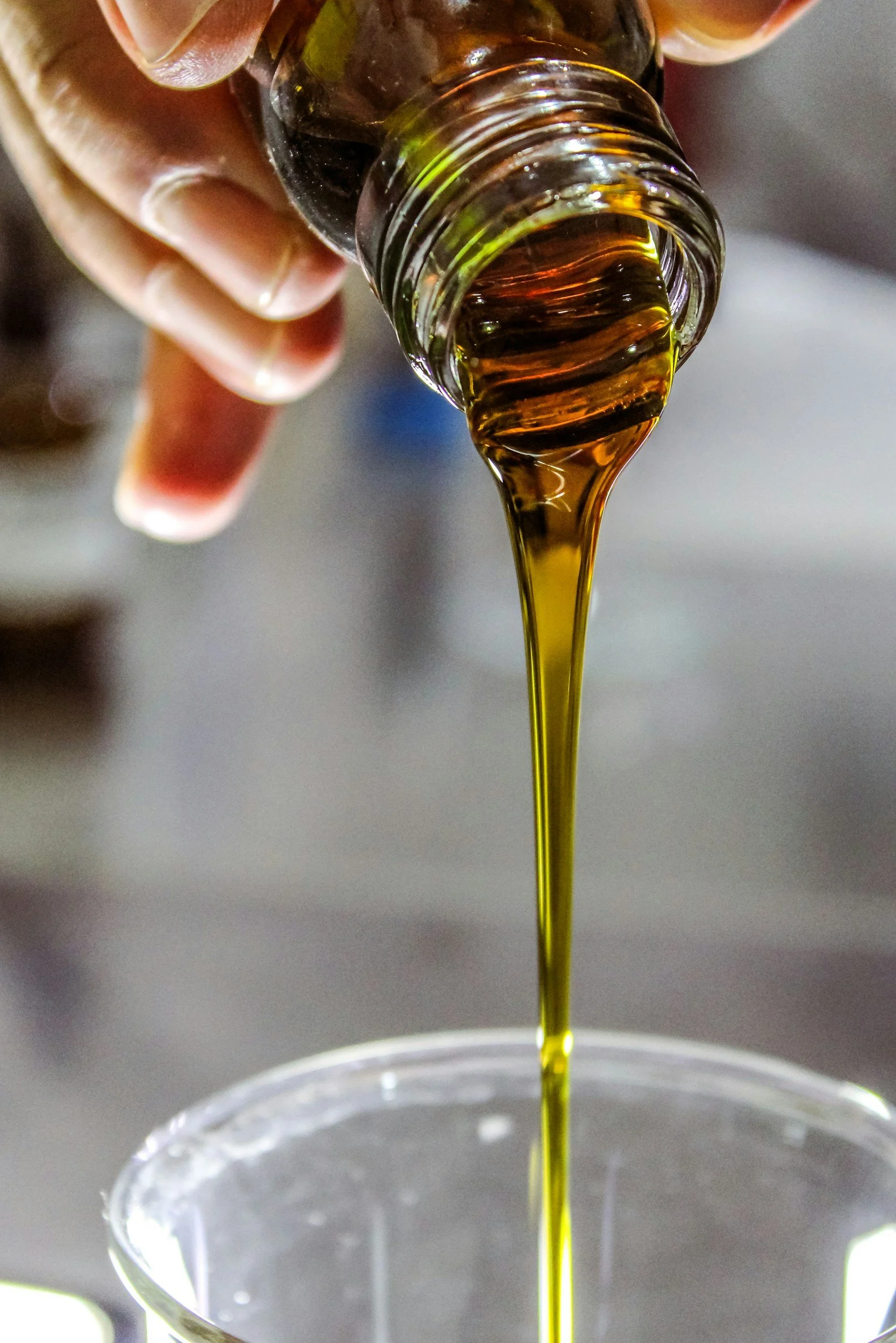 Close-up of a hand holding a small glass bottle pouring honey into a clear glass container.