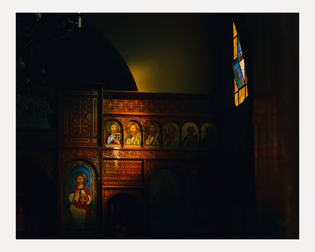 Dimly lit interior of a church with religious icons and stained glass windows, featuring a prominent icon of Jesus Christ.
