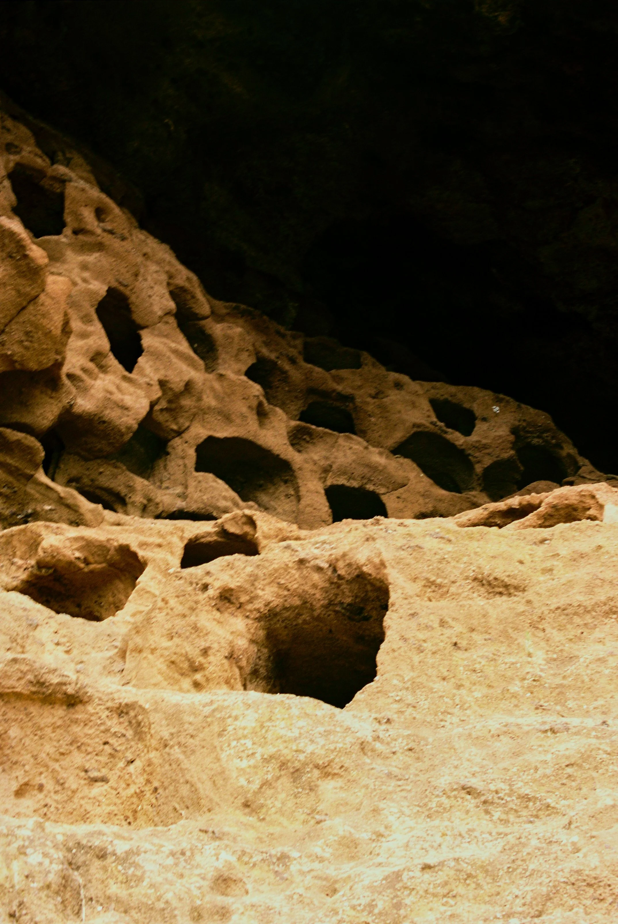Close-up of weathered, porous sandstone rocks inside a cave with dark shadows in the background.