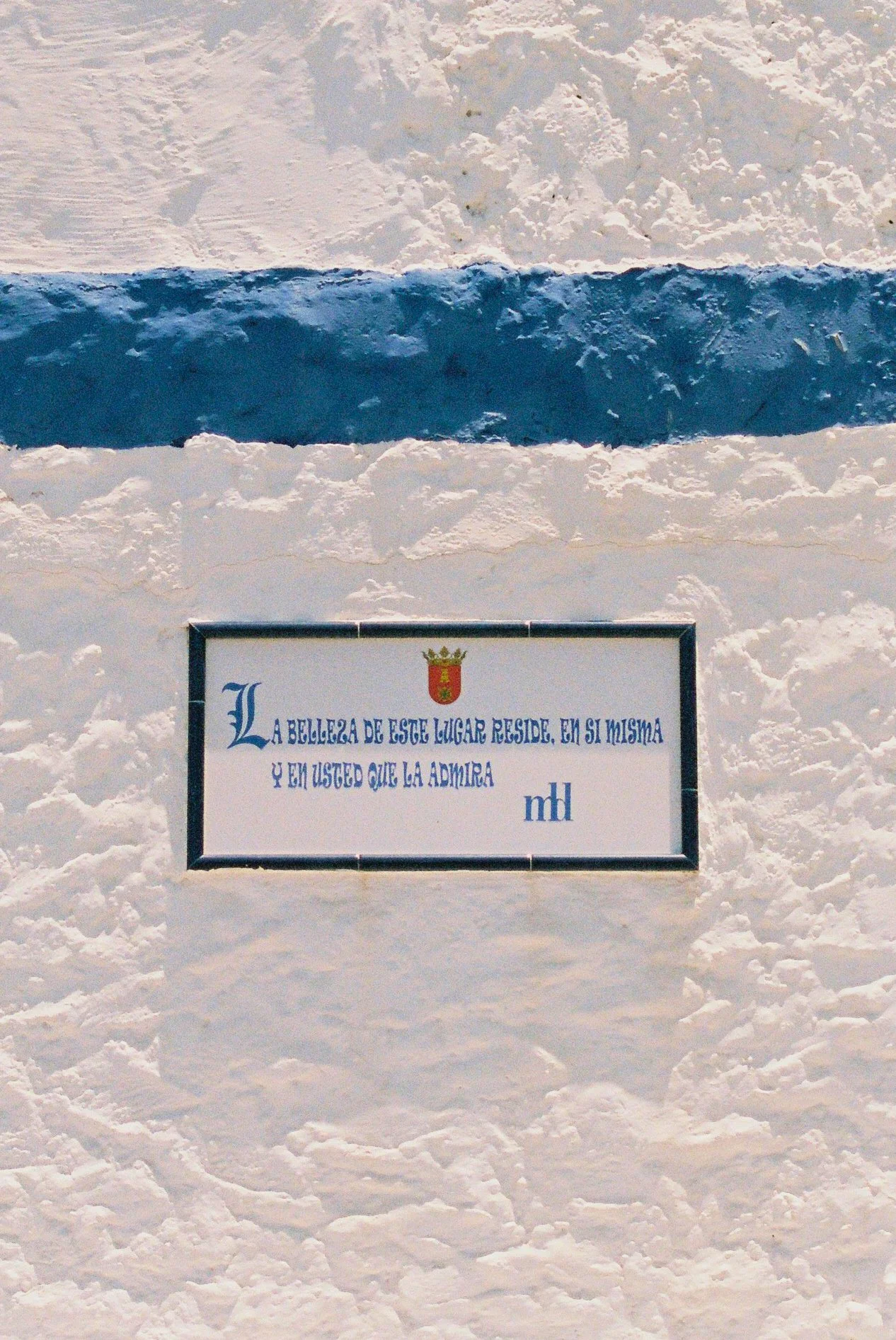 A white snow wall with a plaque featuring a crest and a Spanish inscription that reads: "La belleza de este lugar reside en si misma y en usted que la admira."