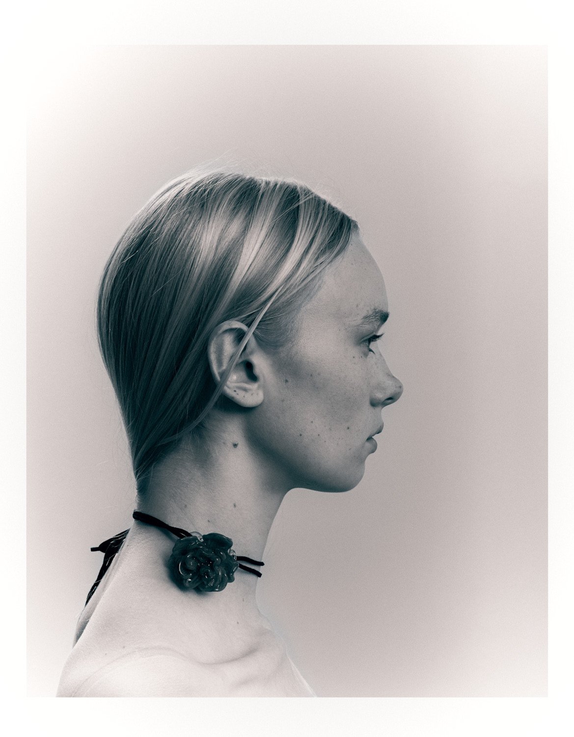 Black and white profile portrait of a woman with long hair and a floral choker necklace.