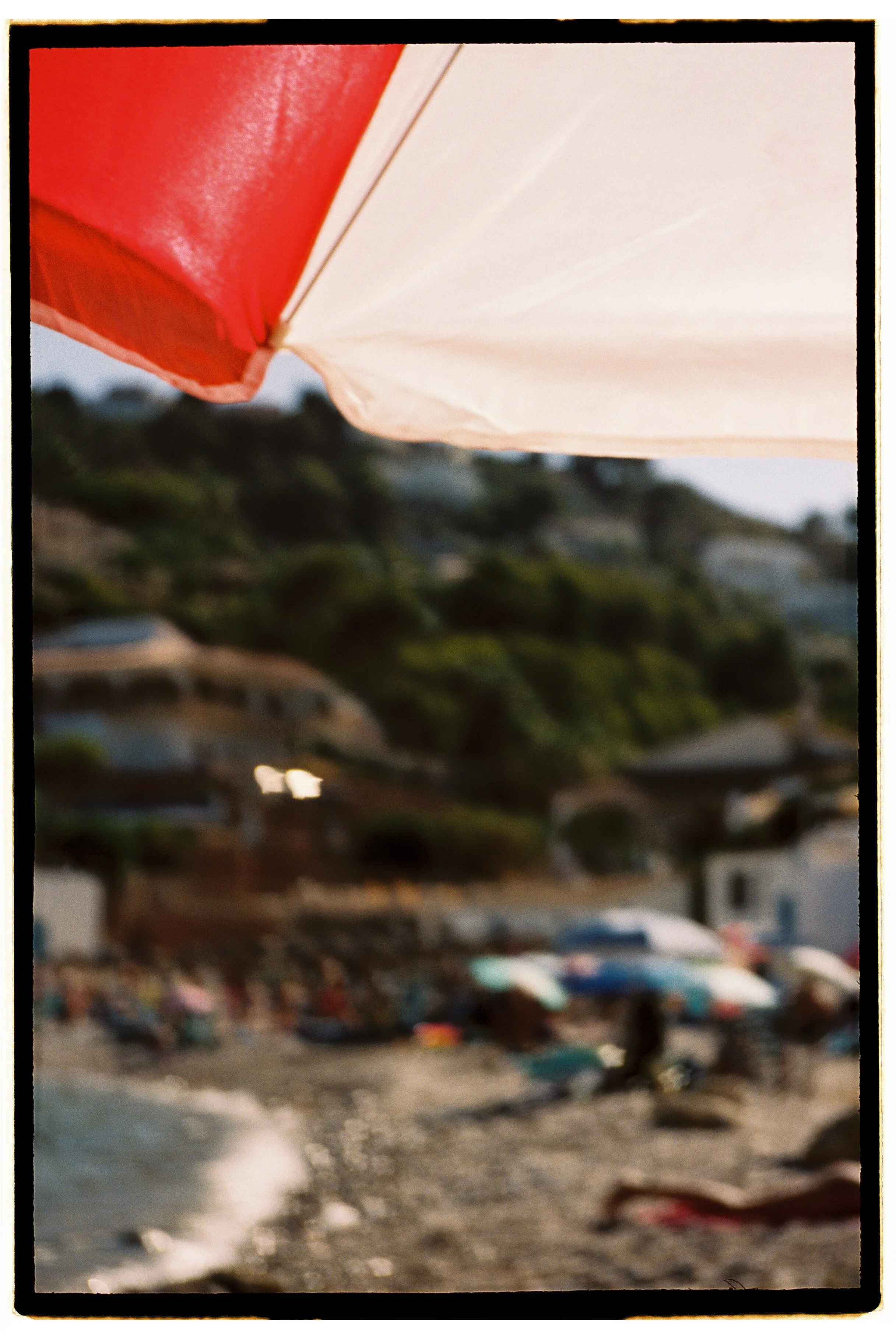 Close-up of a beach umbrella with blurred beach scene and hillside in the background.