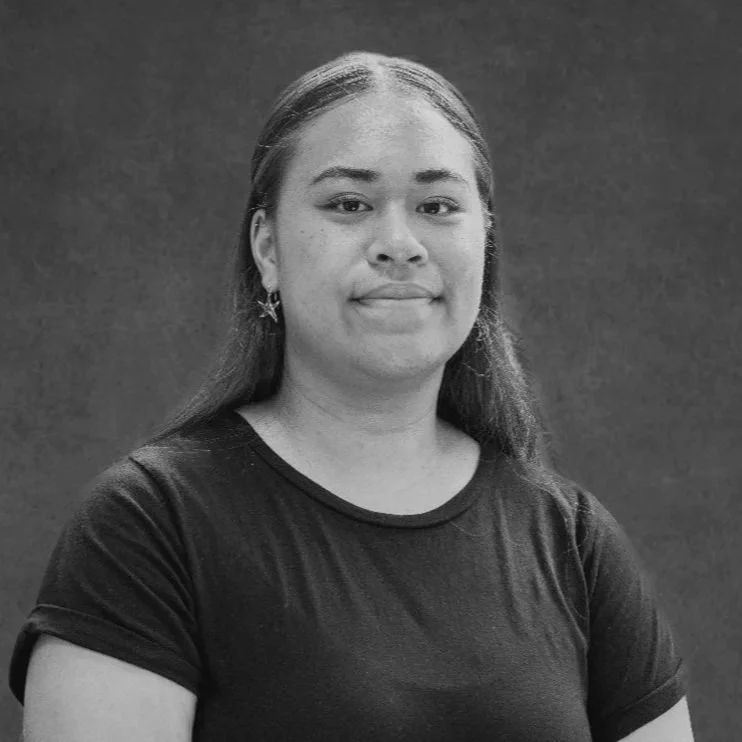 Black and white portrait of a young woman with long straight hair, wearing a black t-shirt and star-shaped earrings, standing against a plain background.